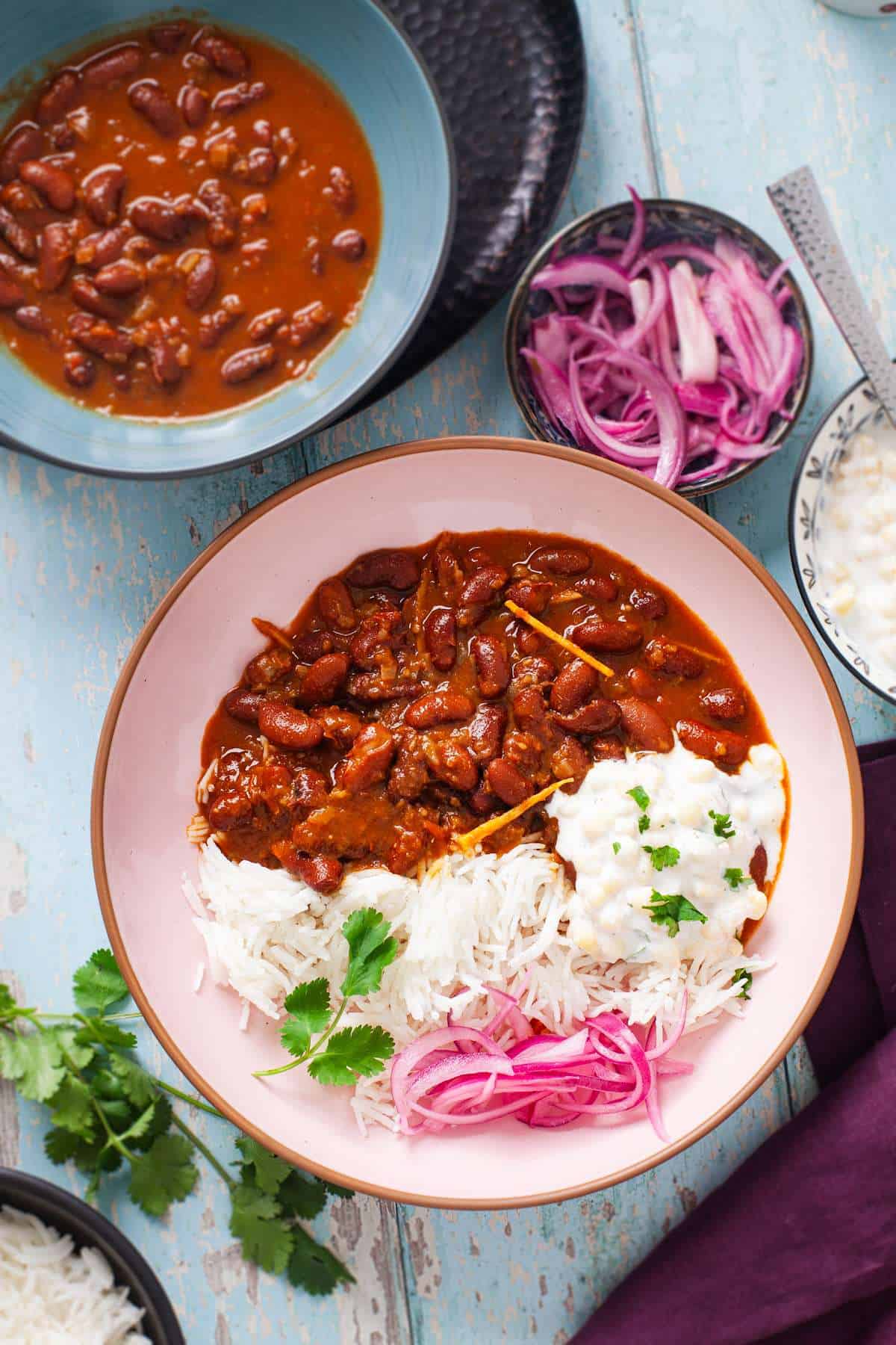 Rajma Chawal in a pink plate with onions and raita.