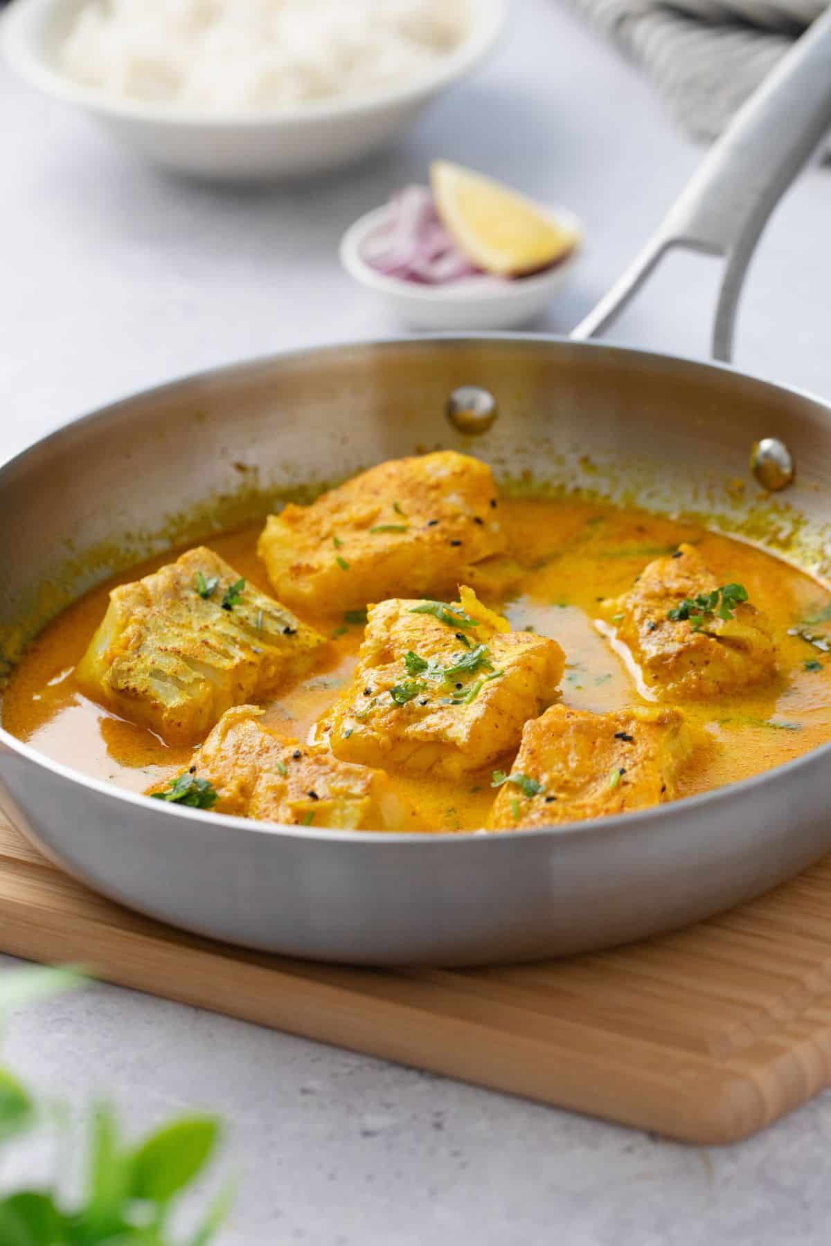 Cod curry served in a stainless steel skillet with rice in background.