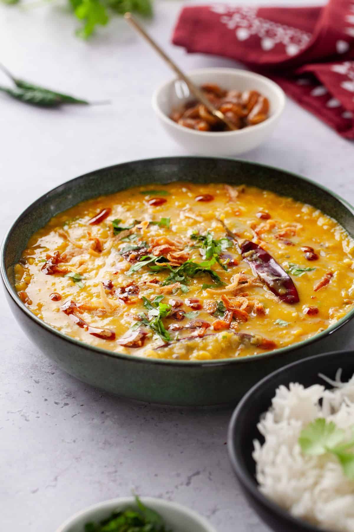 Side image of tarka dal in a green bowl with pickle in background.
