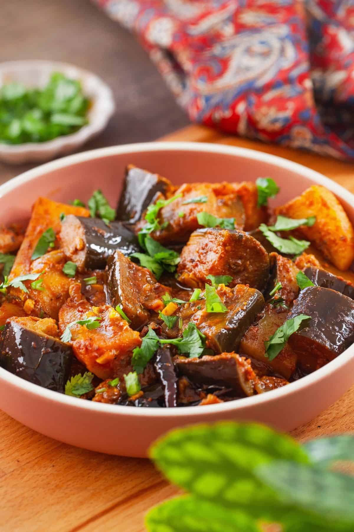 Side view of eggplant and potato curry in a pink bowl.