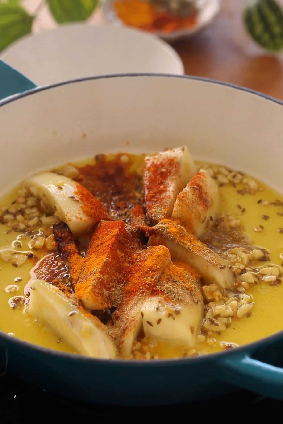 Potatoes added to hot oil along with some water and ground spices.