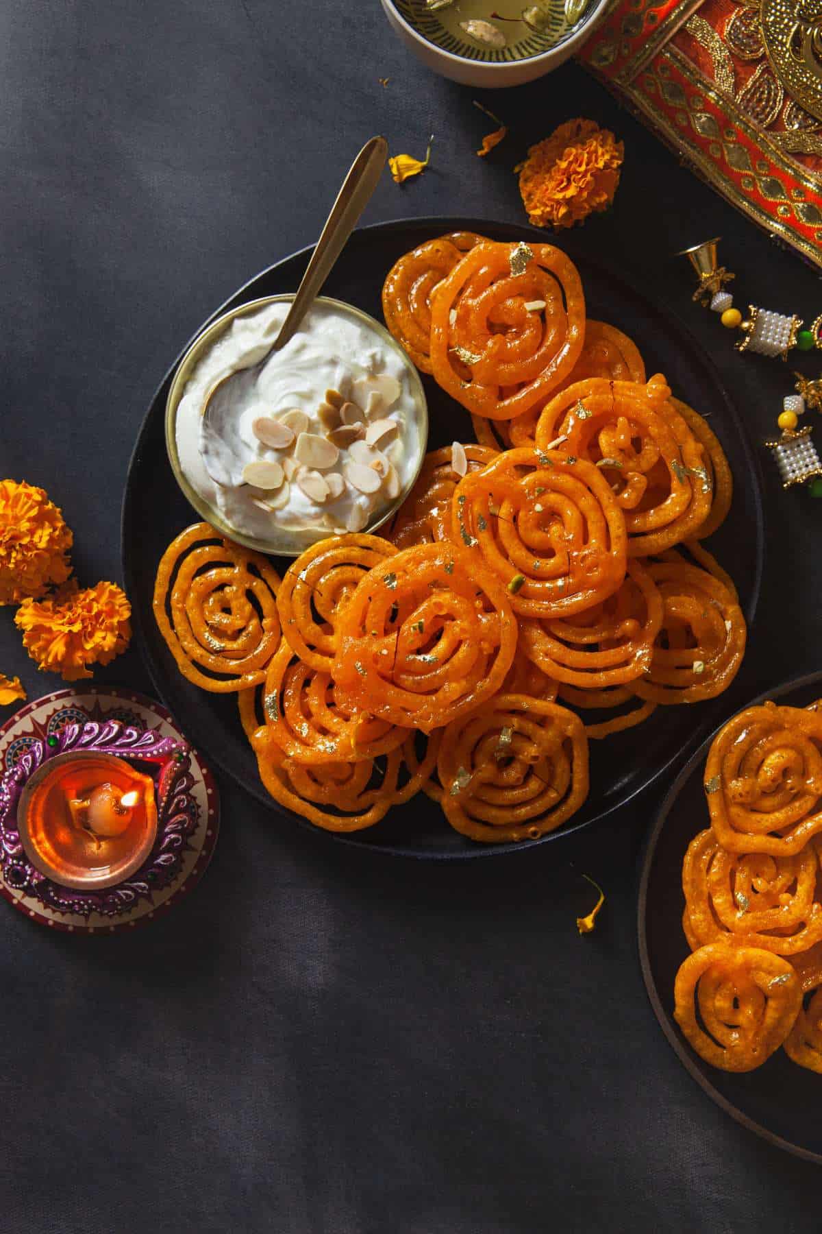 Jalebis served in a black palatter with yogurt. 