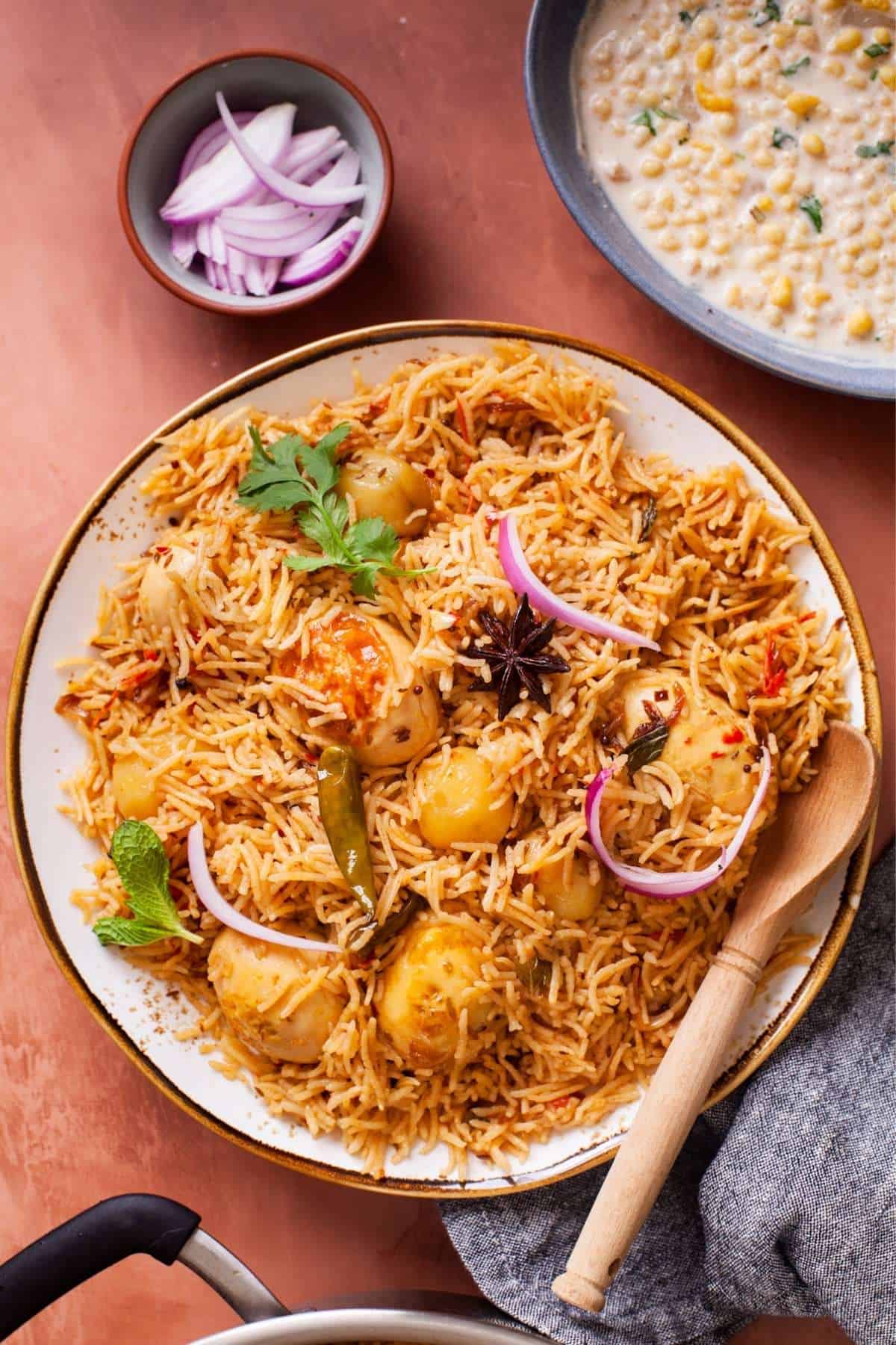 Egg Pulao served in a white plate with raita and sliced onions.