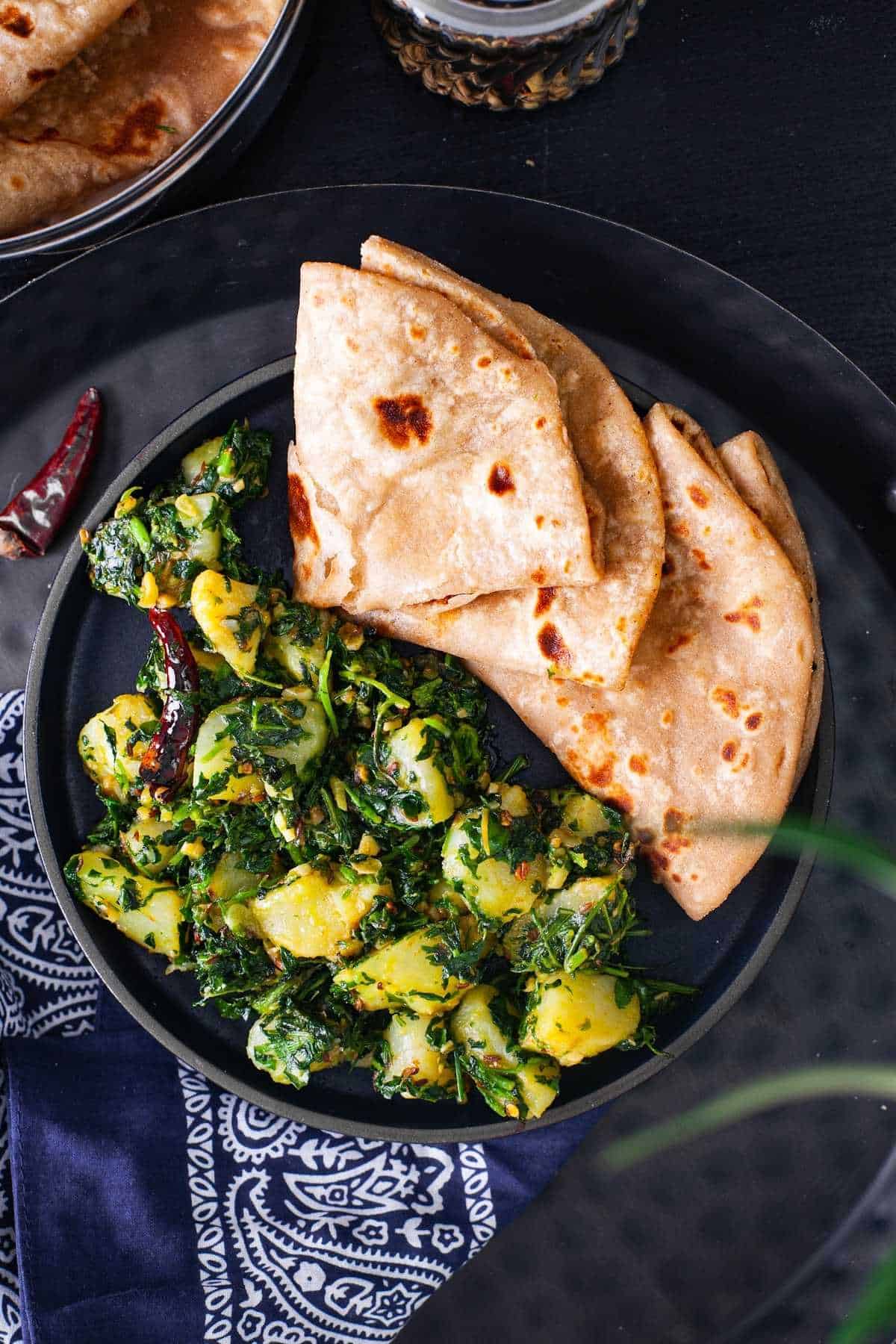 Aloo methi ki sabji served with plain parathas in a black plate. 