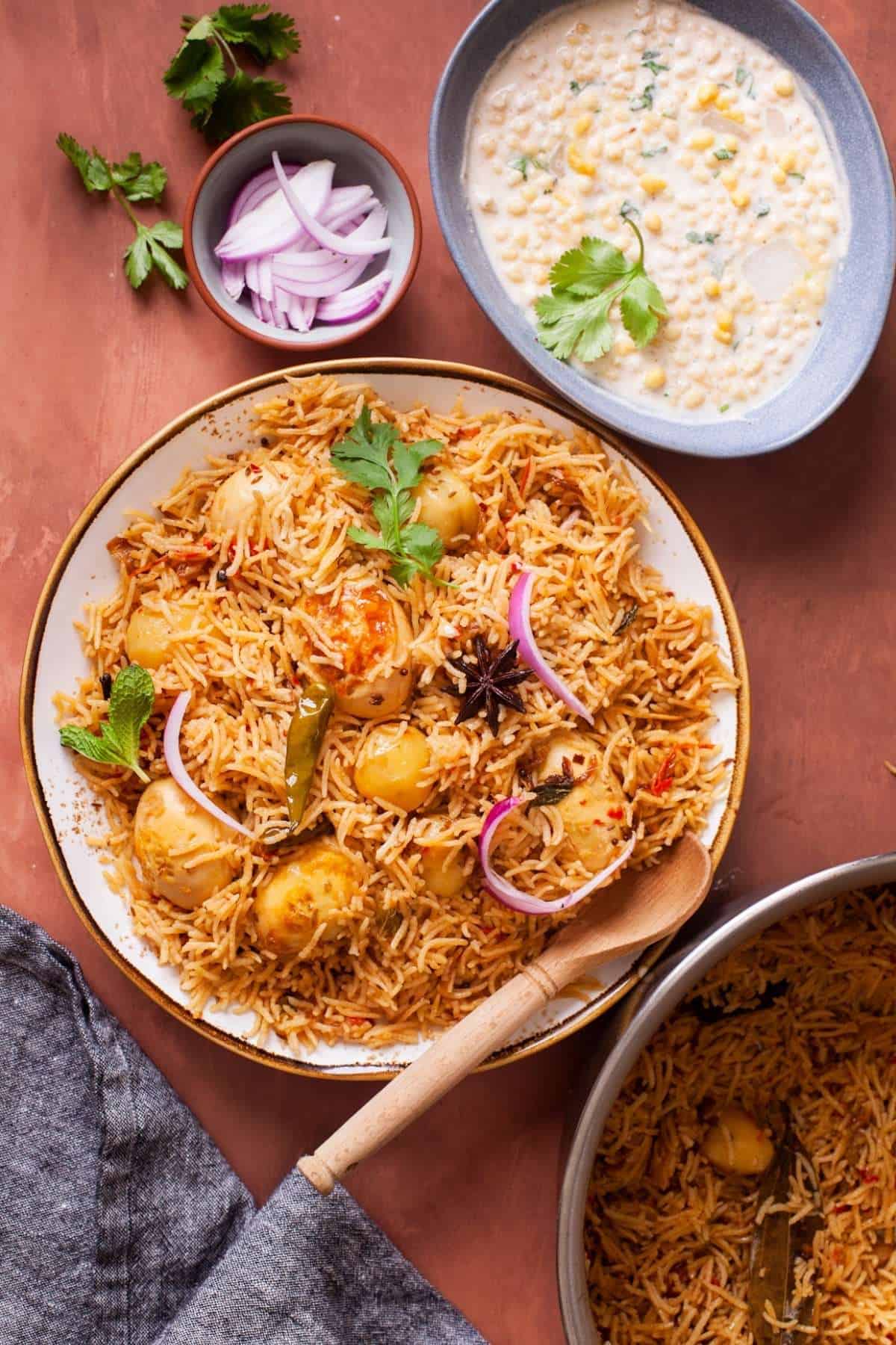 Egg Pulao served in a white plate with bondi raita and sliced onions.