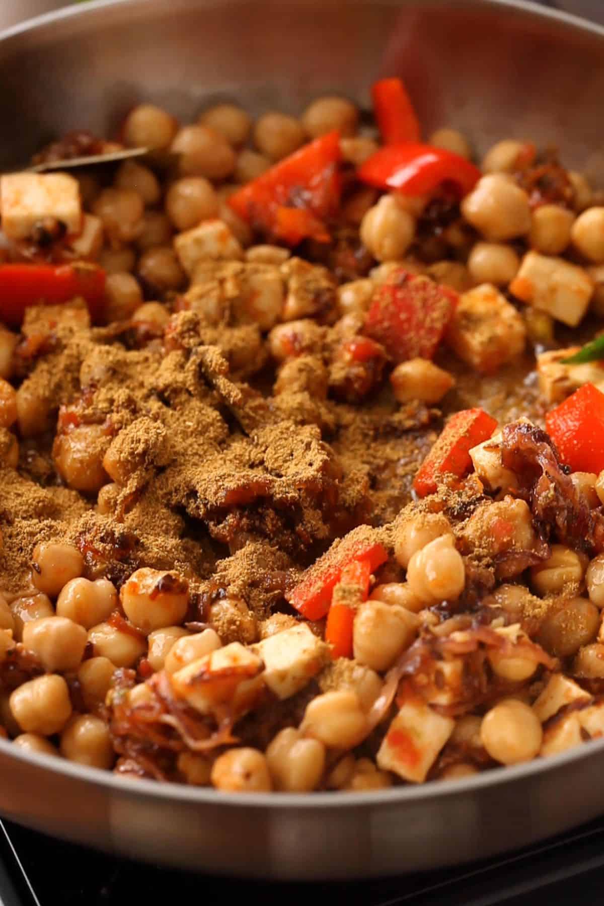 Boiled chickpeas and spices are added to the skillet.