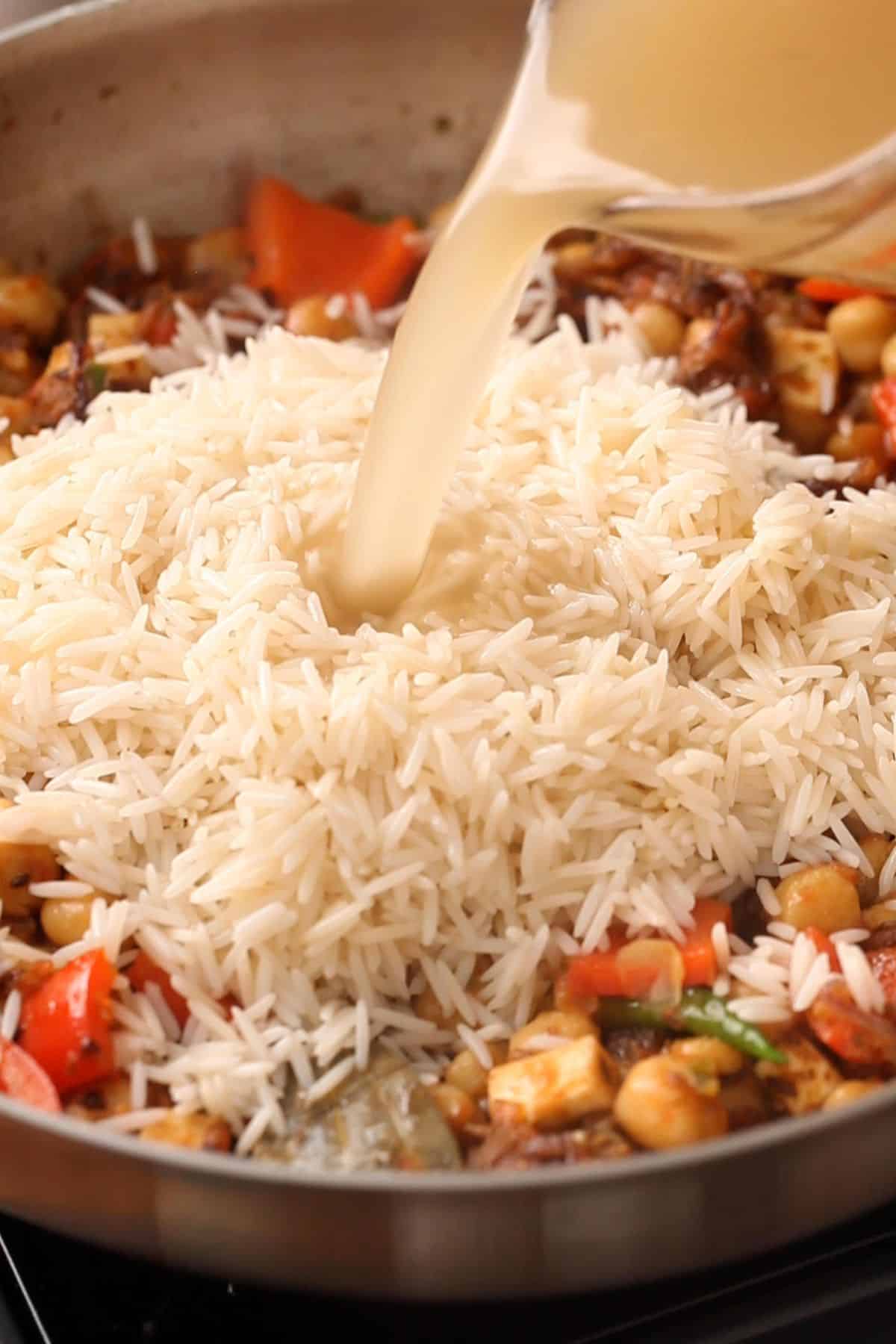 Soaked rice and chickpeas stock is added to the skillet. 