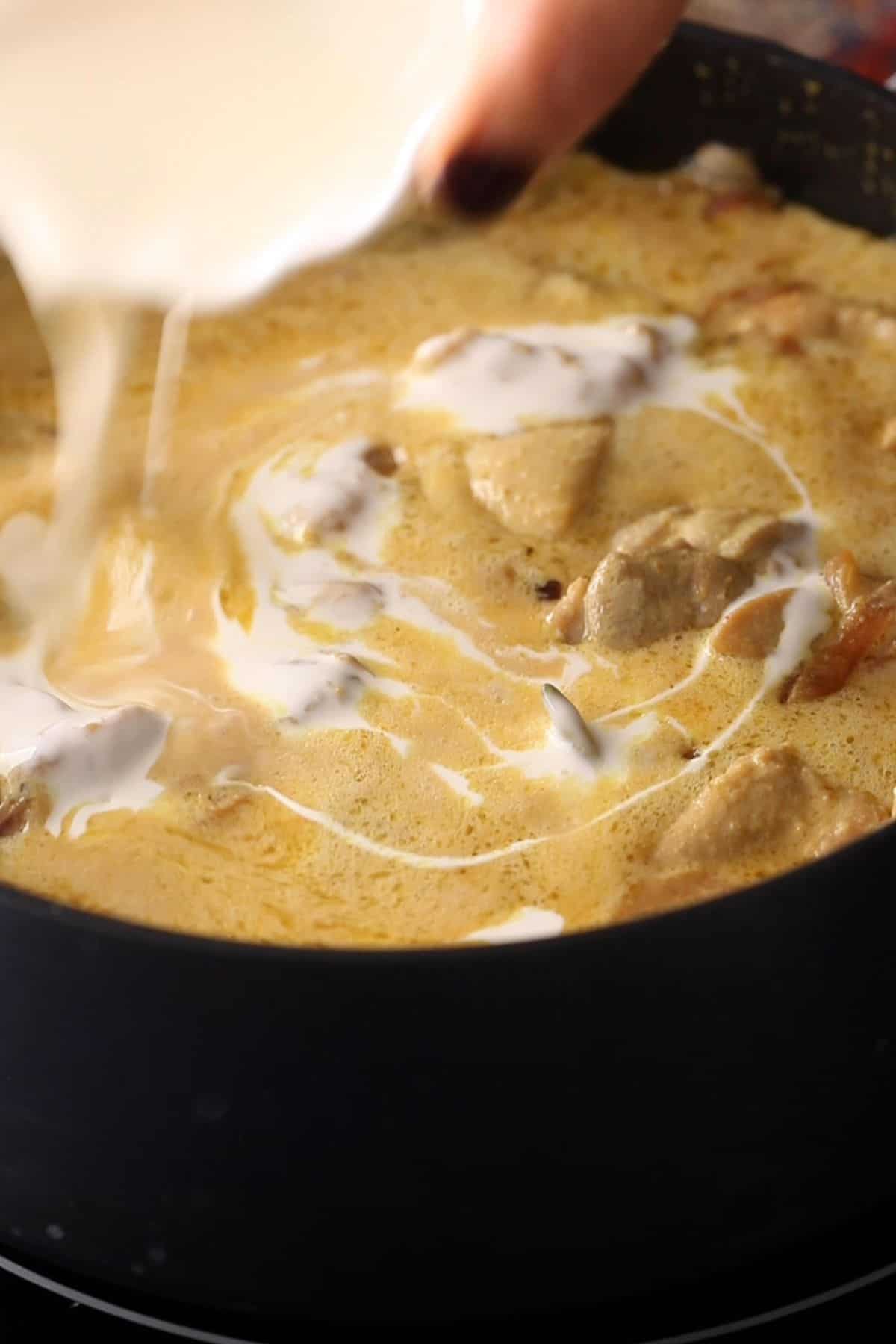 Heavy cream is poured over the chicken korma.