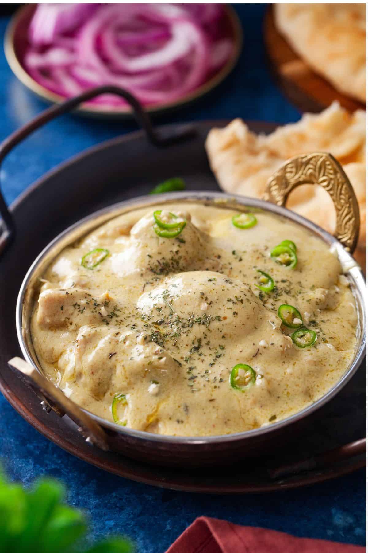 White Chicken Korma served in a steel wok with naan in background.