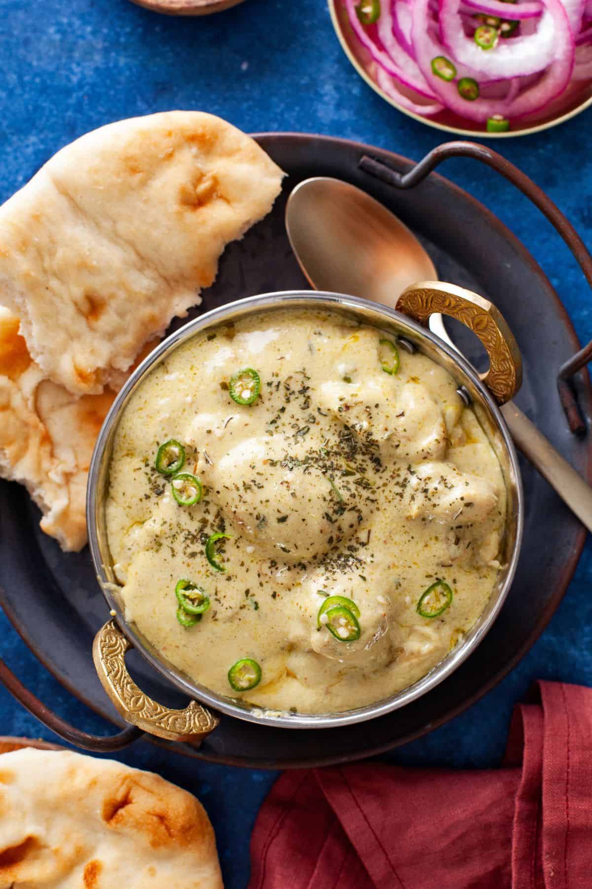 Overhead image of  Chicken Korma served in a steel wok with naan & pickled onions.