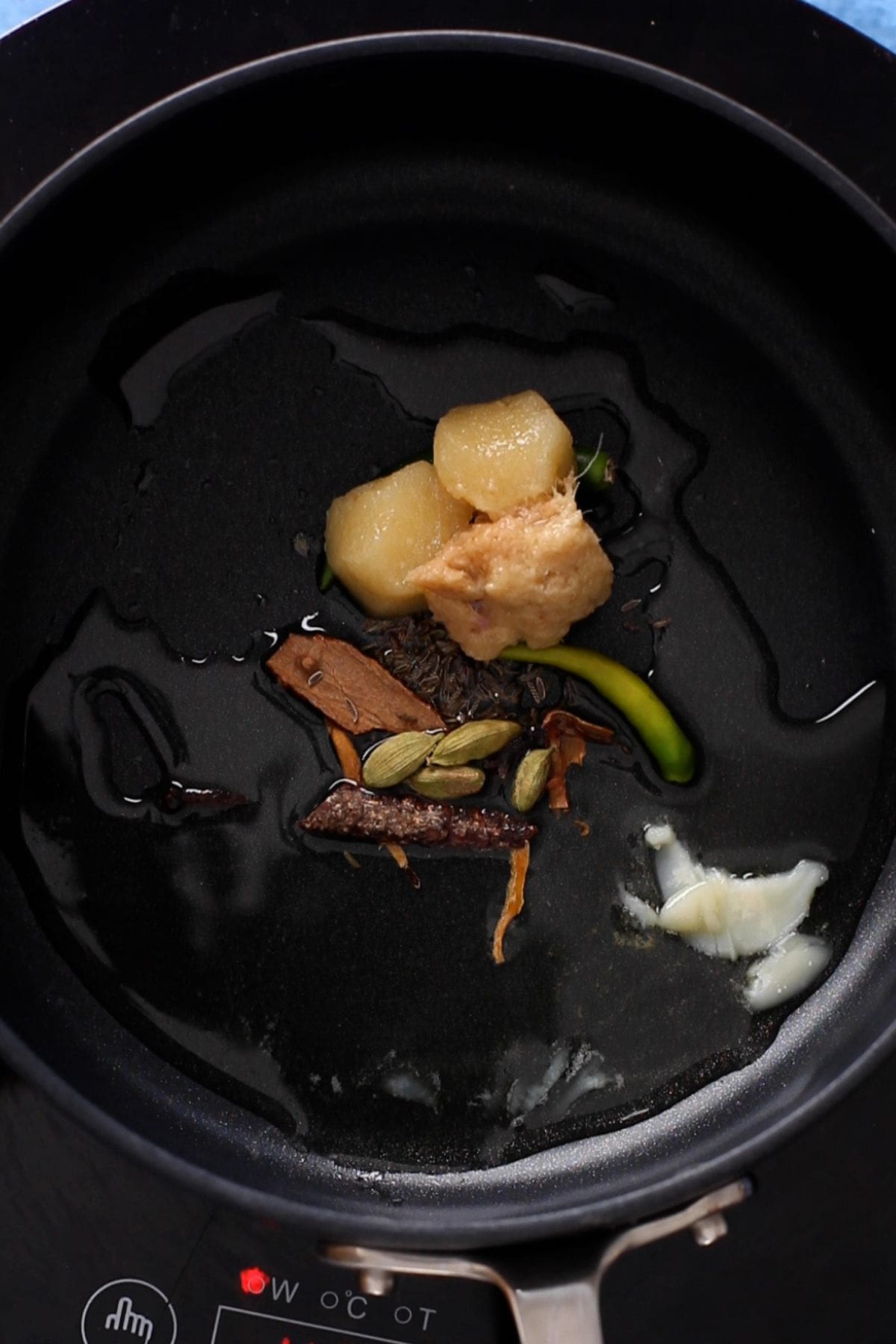 Whole spices, ginger & garlic are added to ghee in a black cooking pot. 