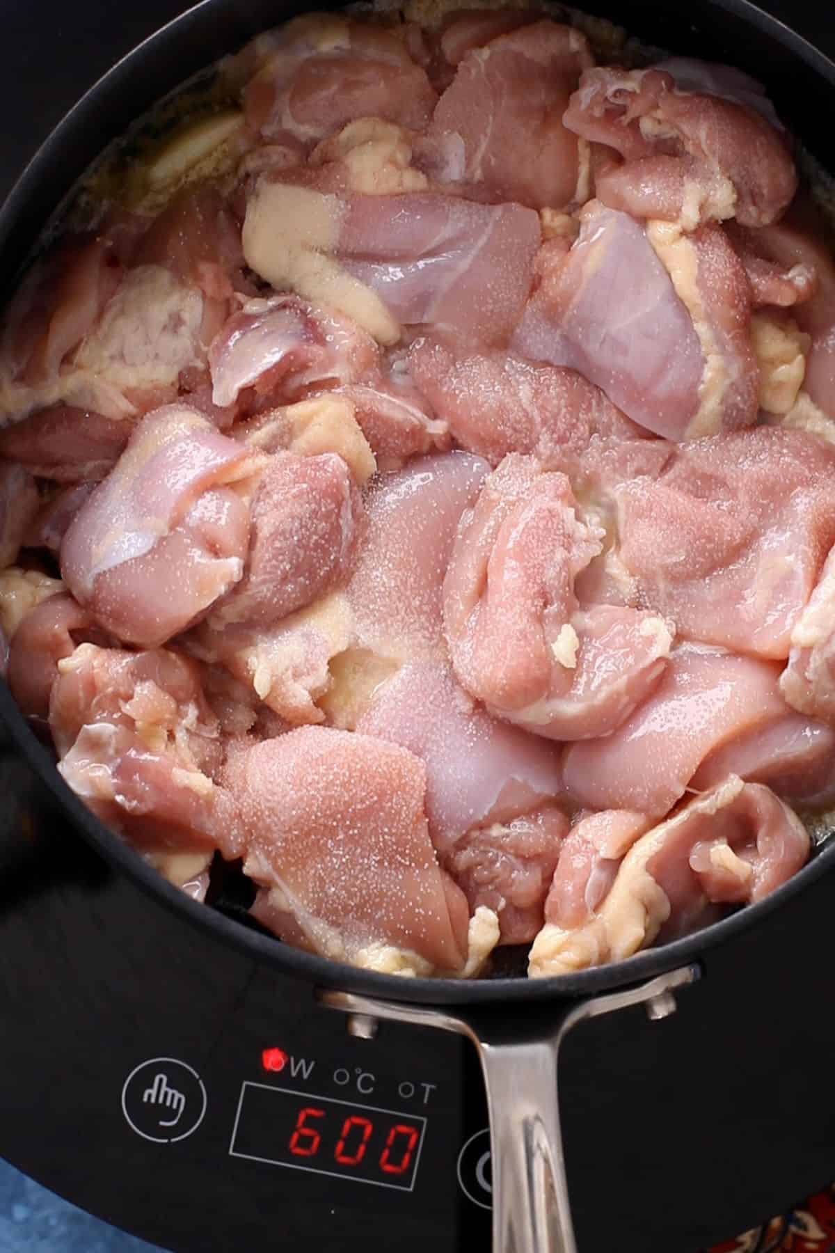 Cut Chicken thighs is added next to the pot along with salt. 