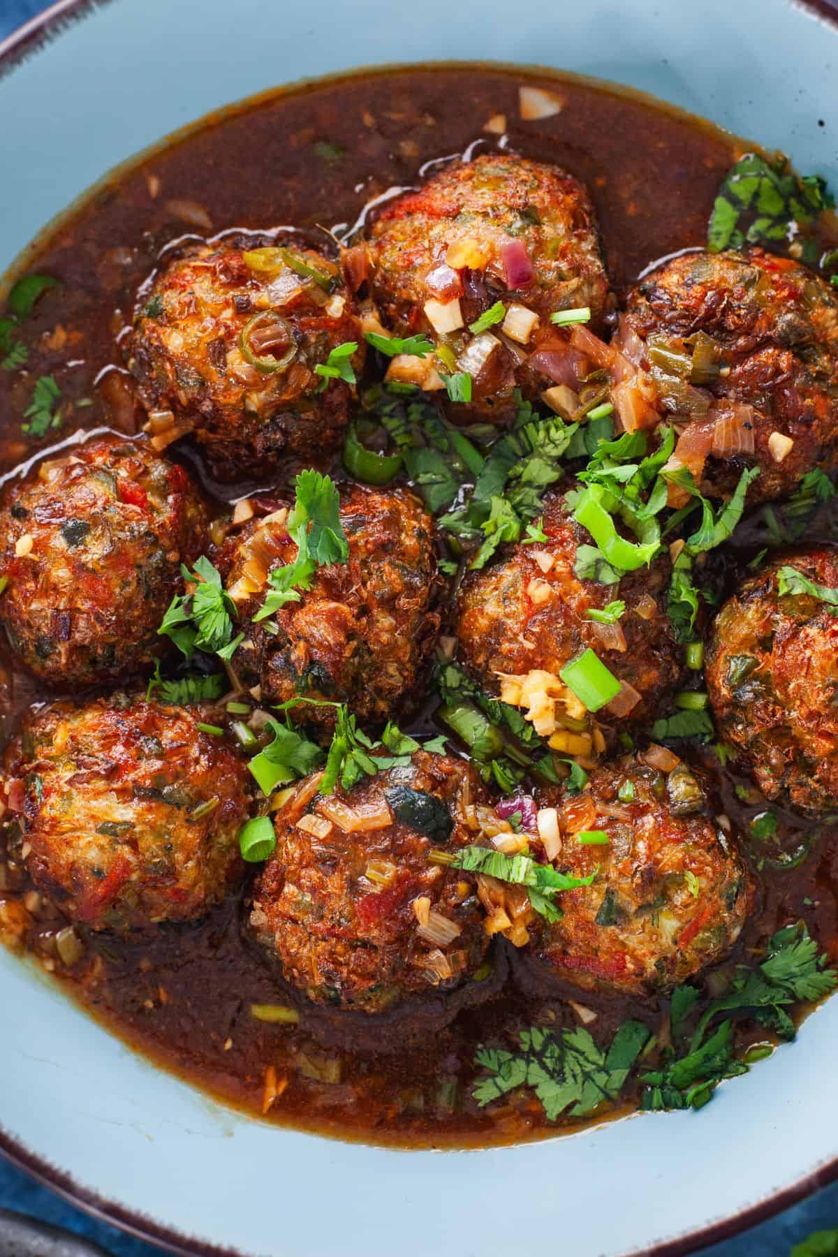 A closeup image of ten round veg balls submerged in a spicy & tangy manchurian gravy.