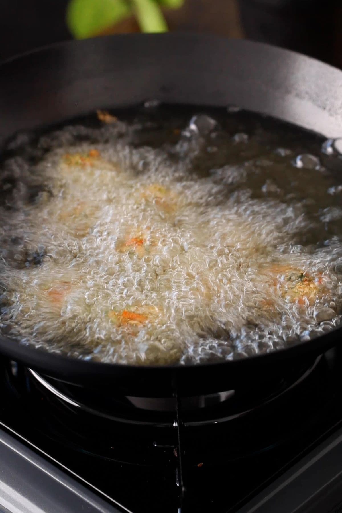 Veg dumplings are fried in hot oil in balck wok. 