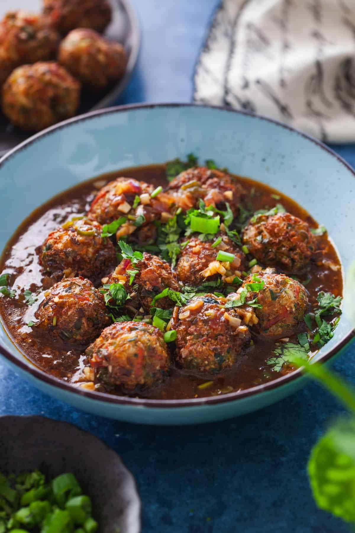 Vegetable Manchurian served in a blue bowl with white & black napkin in background.