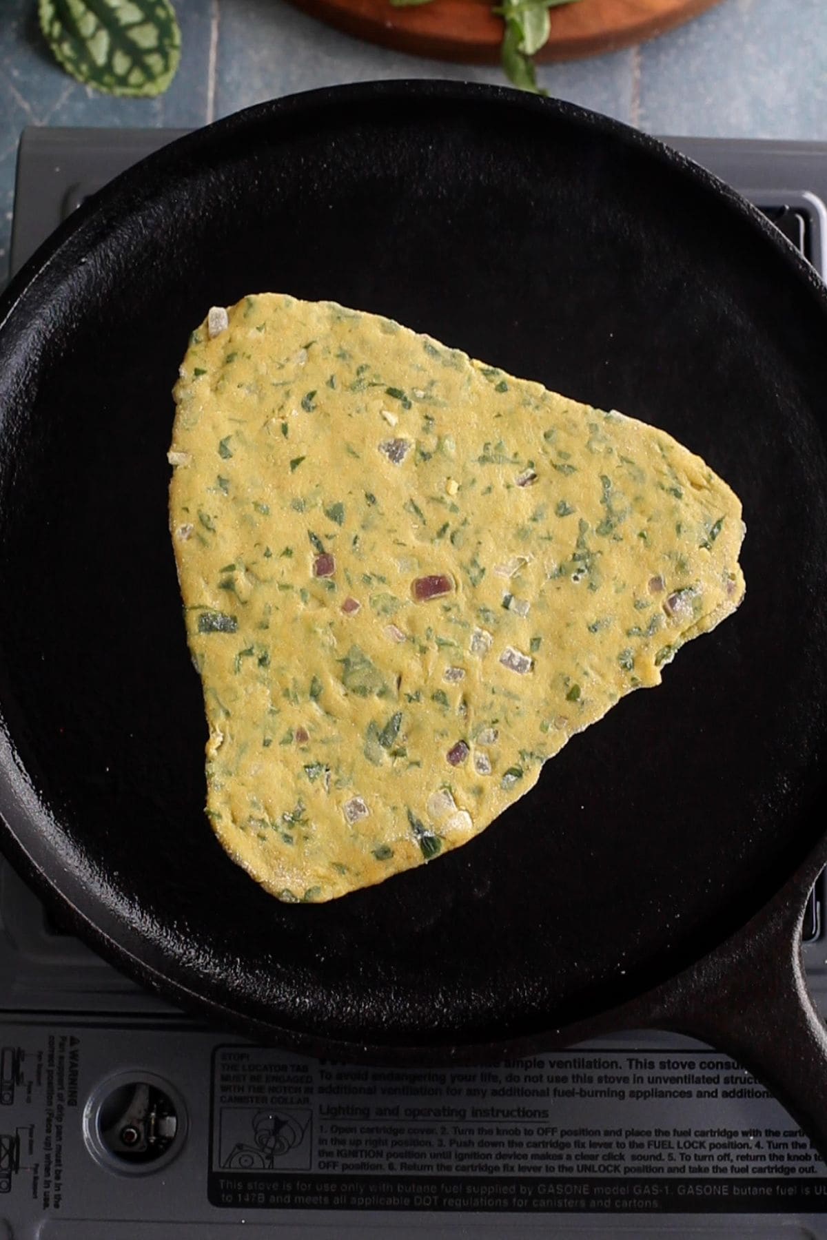 Rolled methi paratha is placed on an iron griddle for cooking.