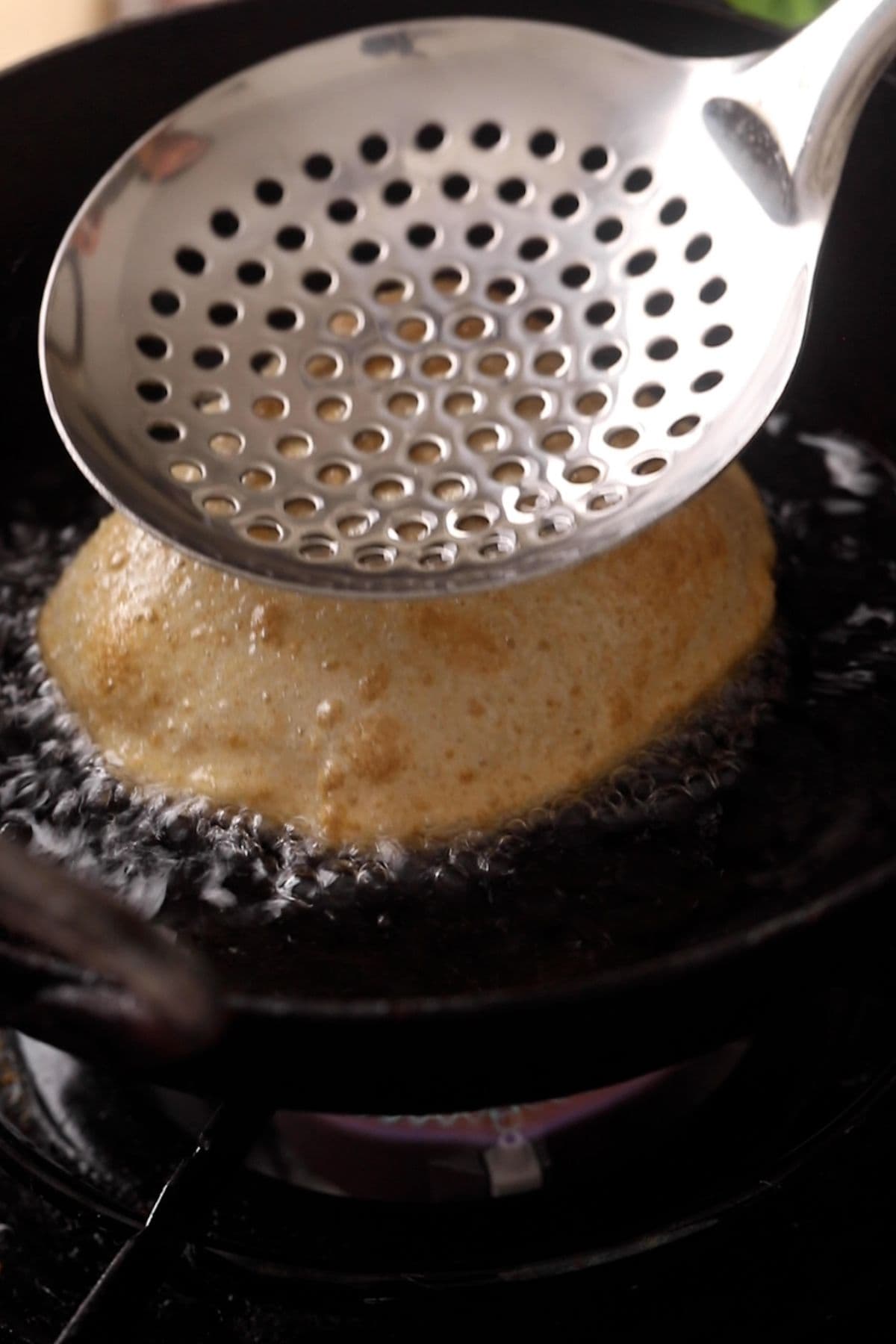 Poori is pressed with a slotted spoon to help it puff.