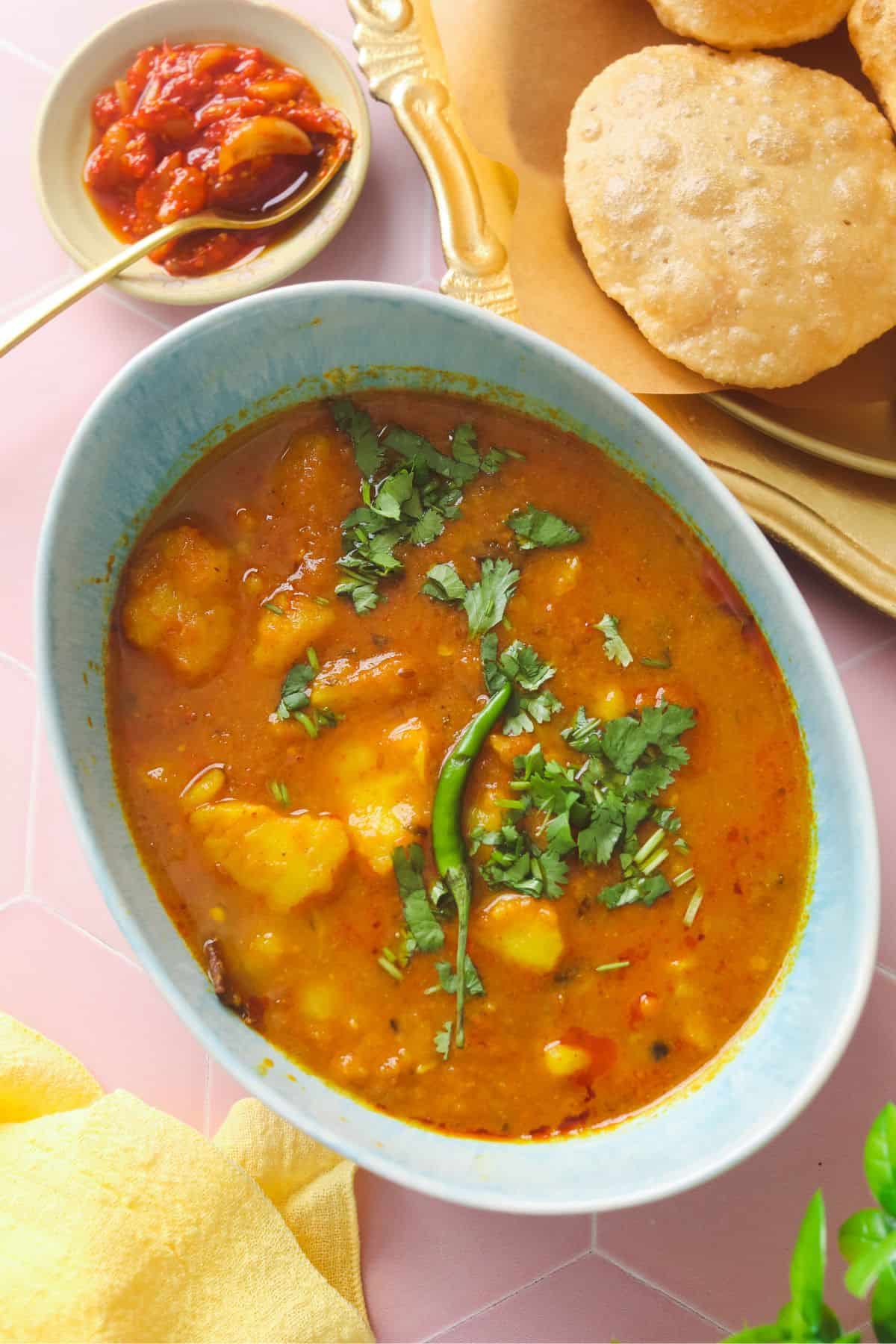 Top view of aloo curry garnished with green chilli and cilantro. 