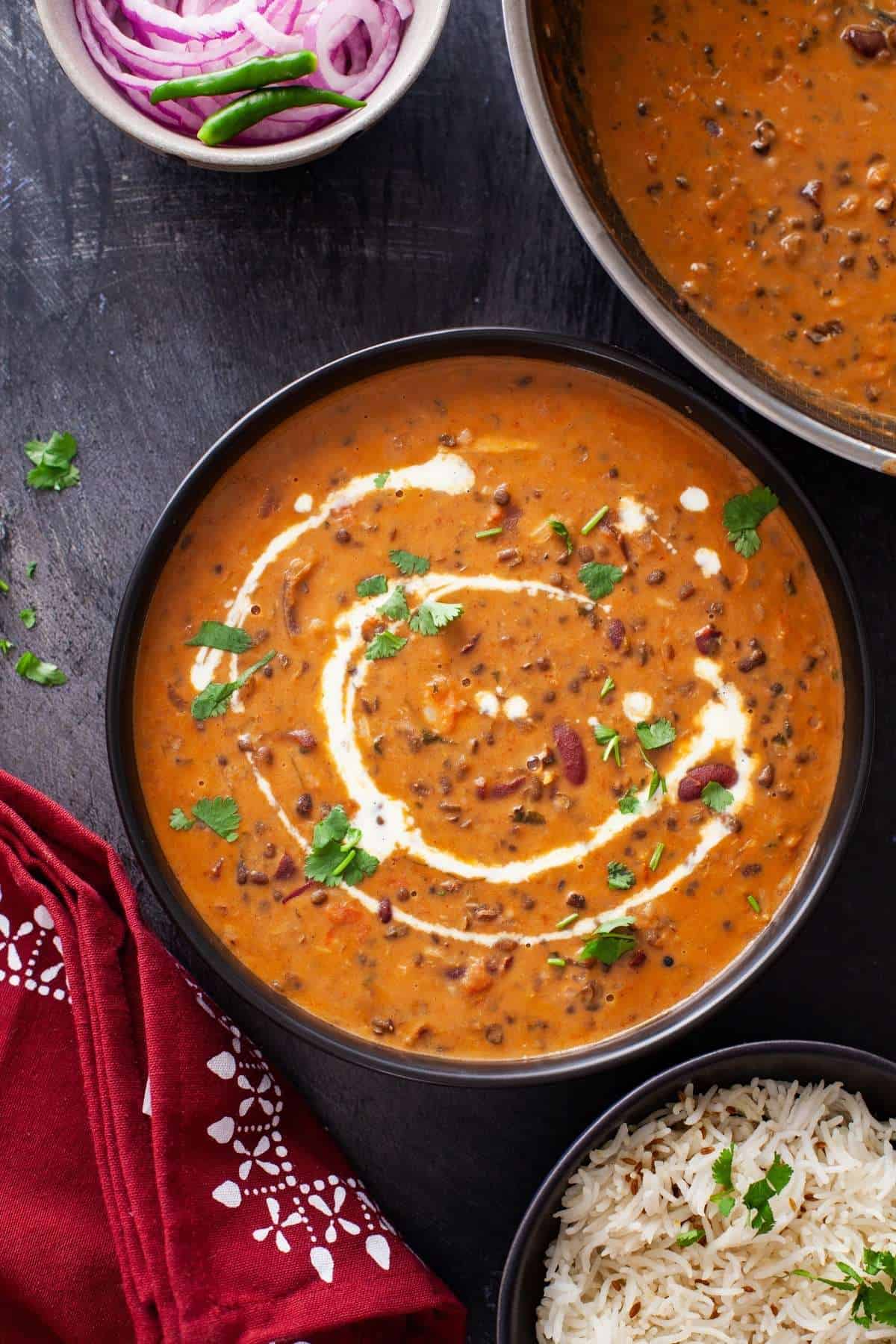 Dal makhani served in a black bowl and plated with rice and onions.