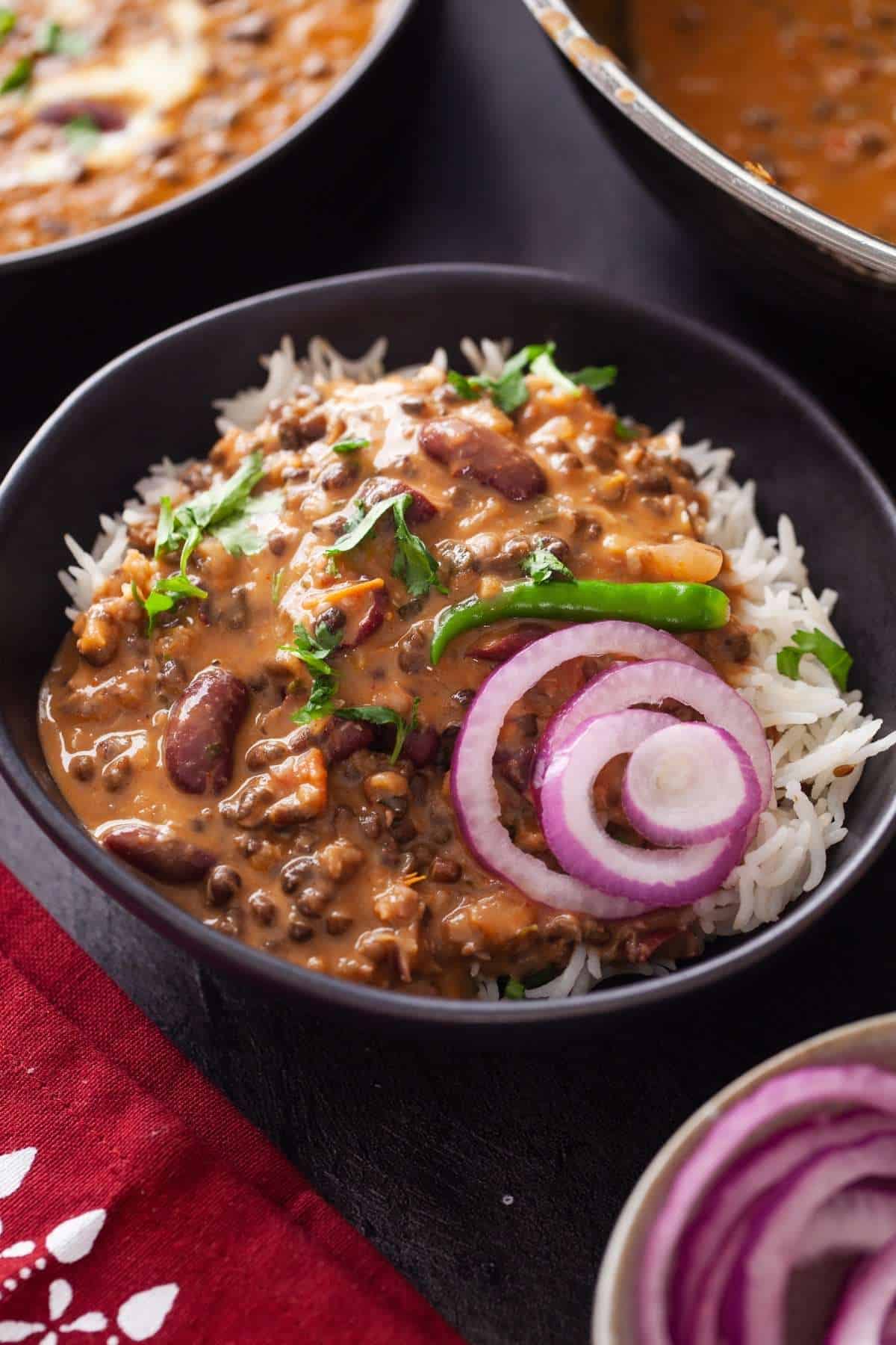 A bowl of rice topped with ladles of makhani lentils, green chili and onion.