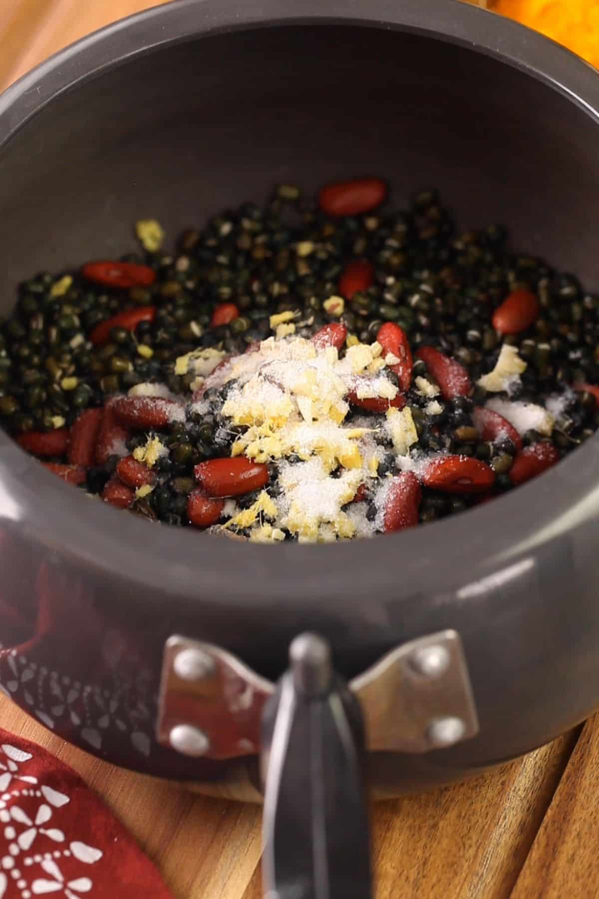 Soaked lentils and beans in a black pressure cooker with spices.