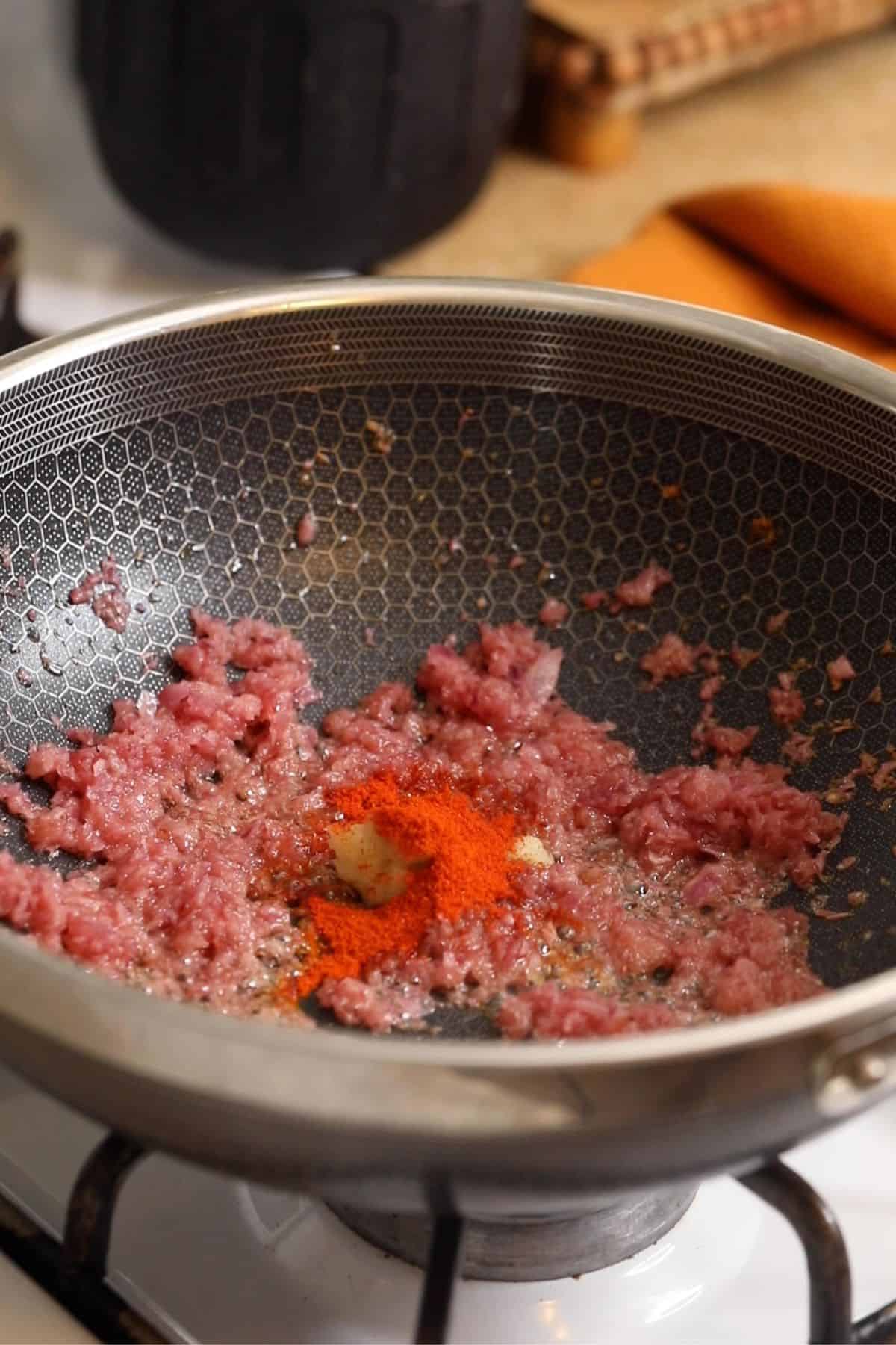 Garlic paste and kashmiri chilli powder are added to onions.