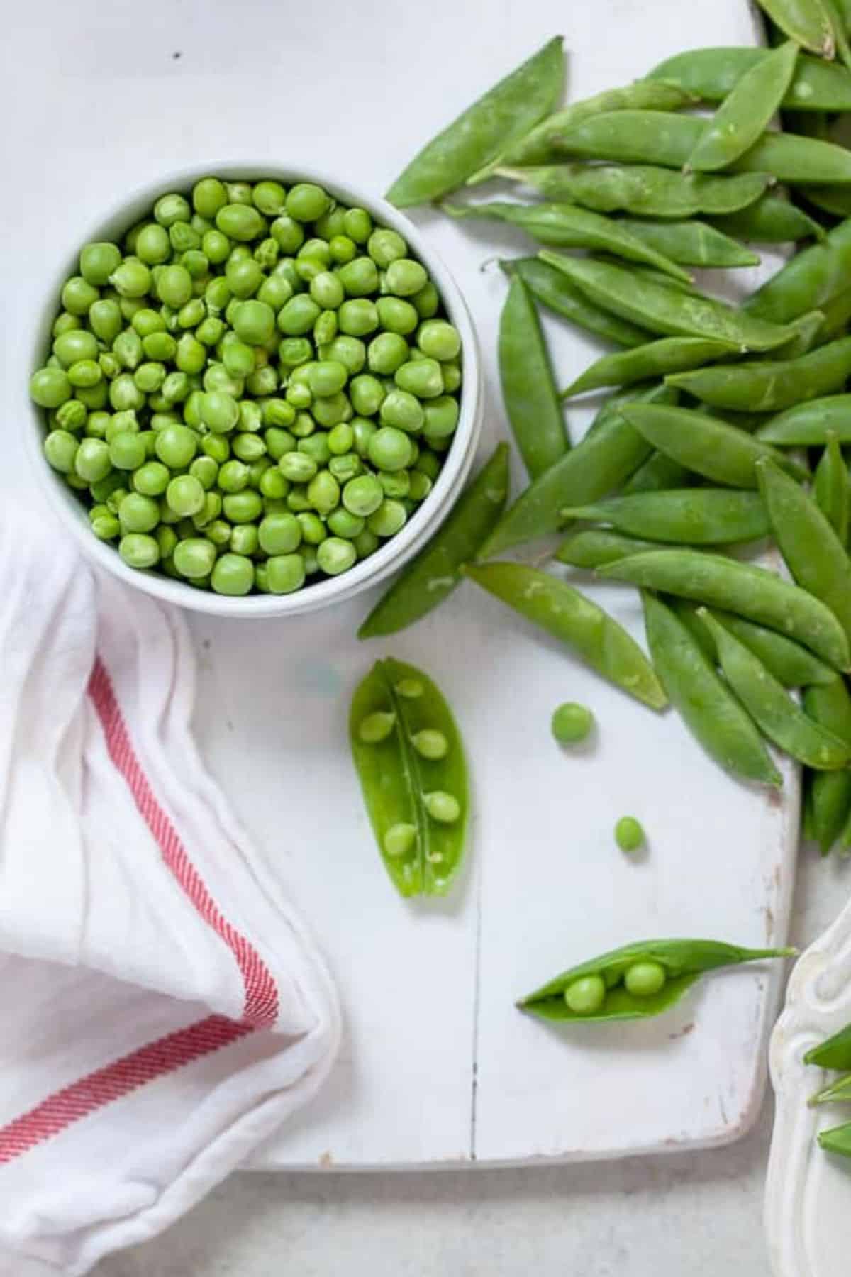 Fresh shelled peas in a white bowl with pea shell on the side.