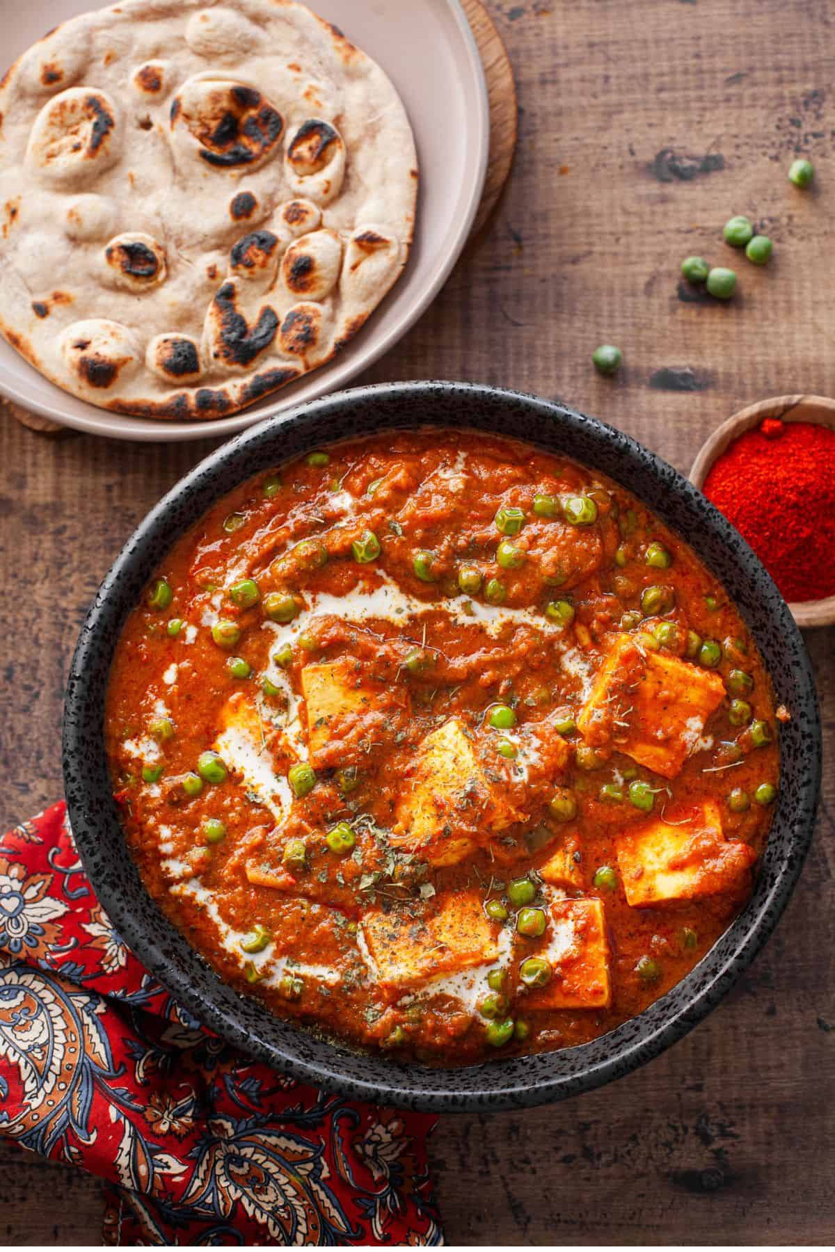 Matar Paneer served in a black bowl with tandoori roti. 