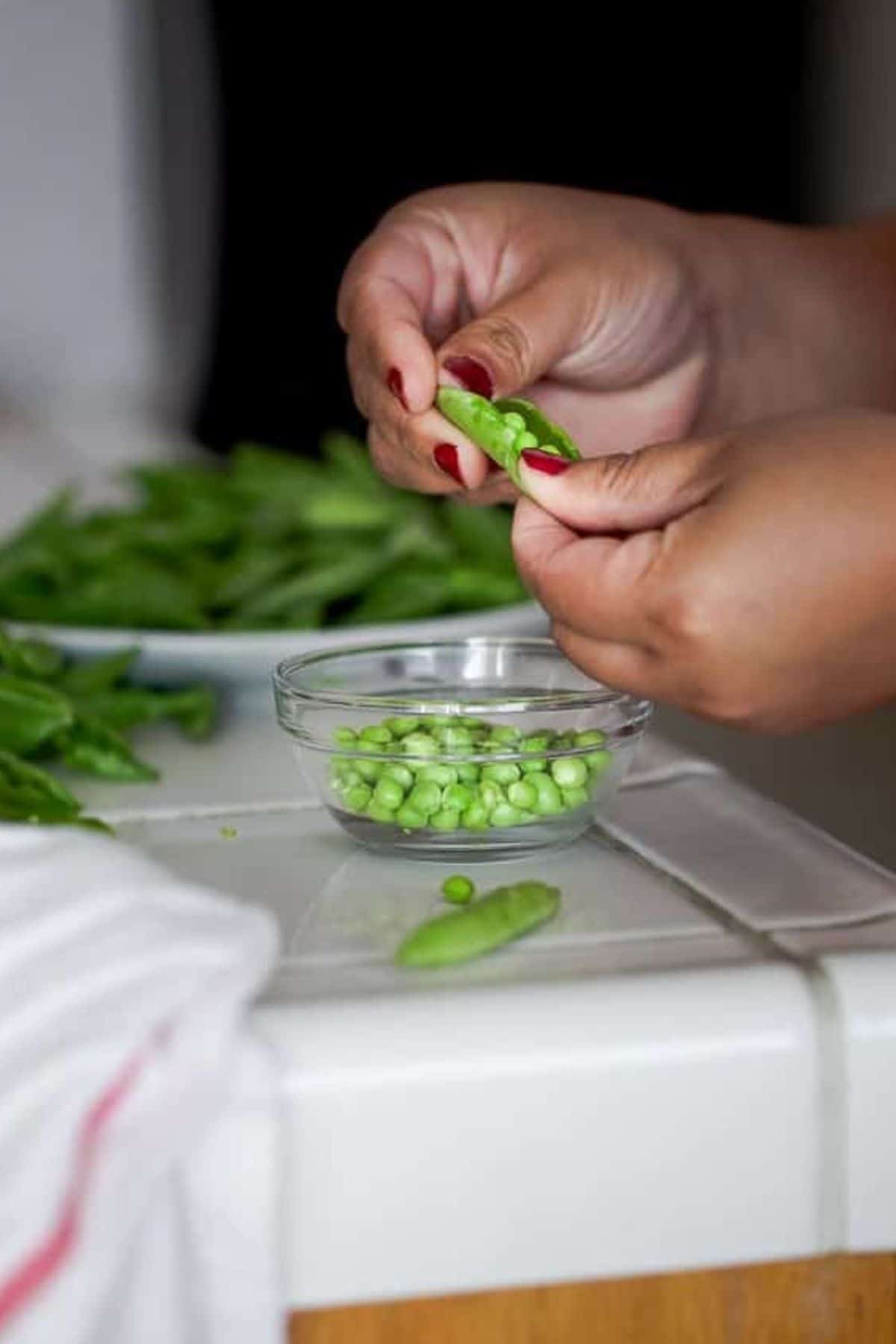 Shelling fresh peas on a white tile kitchen counter. 