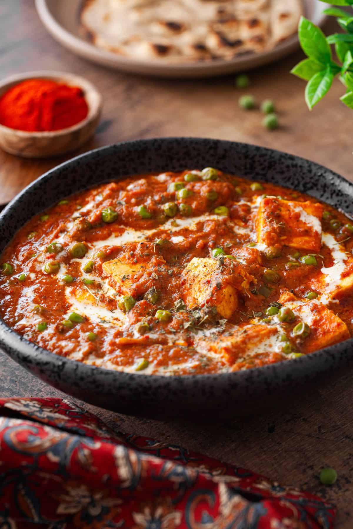Side shot of mutter paneer curry with roti in background.