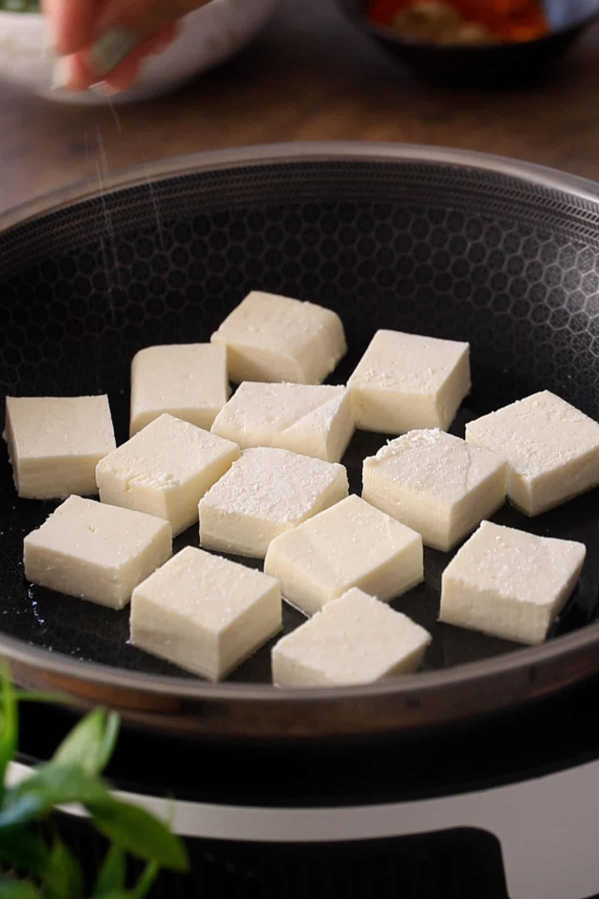 Paneer cubes are placed in a single layer in a black skillet.