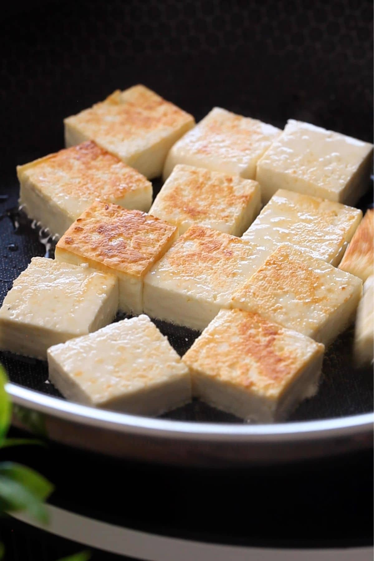 Panfried paneer pieces in a black cooking pan.