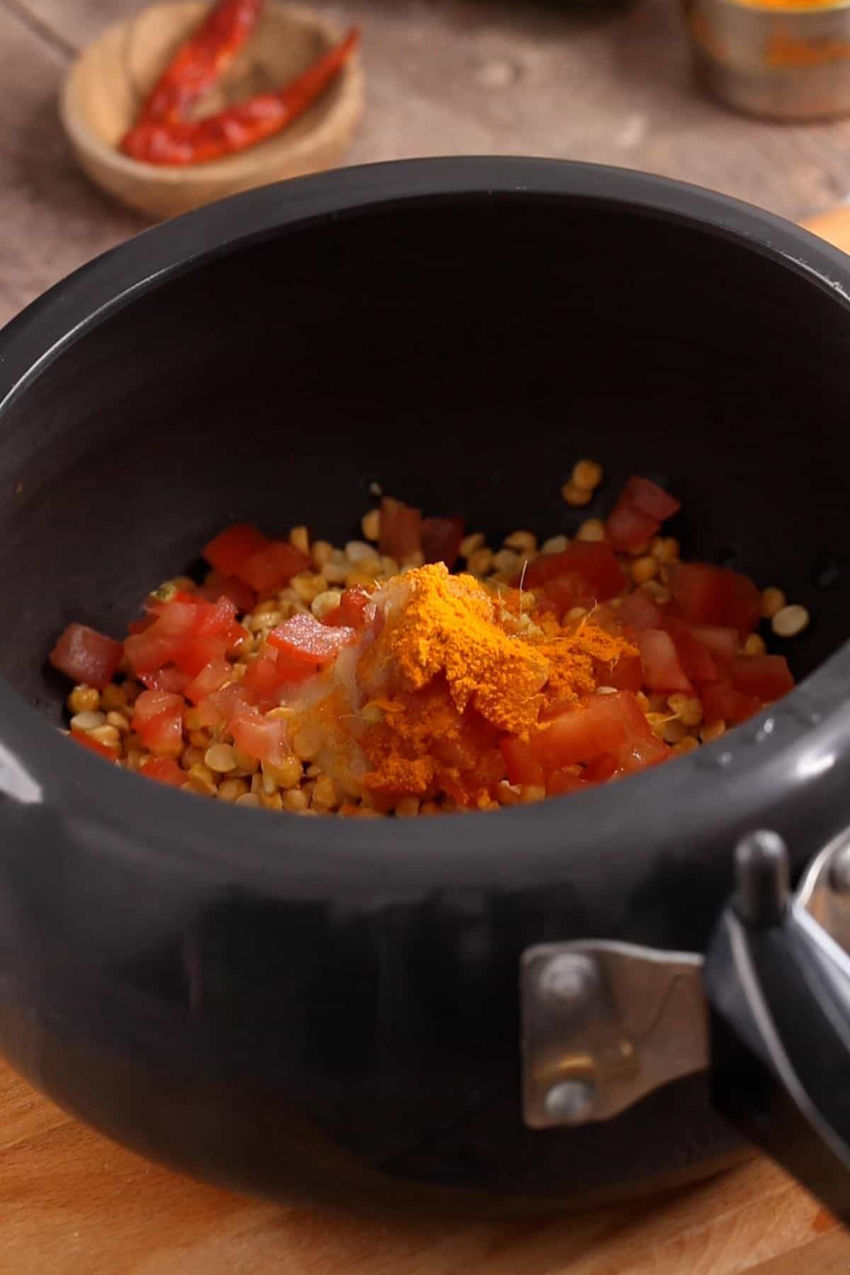 Chana dal with tomatoes, spices in a black pressure cooker.