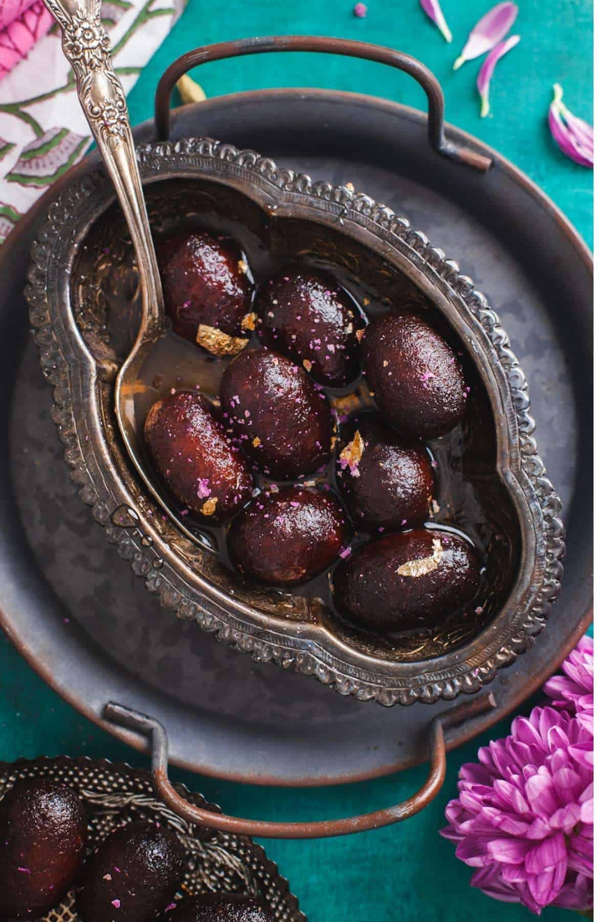 Kala Jamuns soaking in syrup in a silver oval bowl.