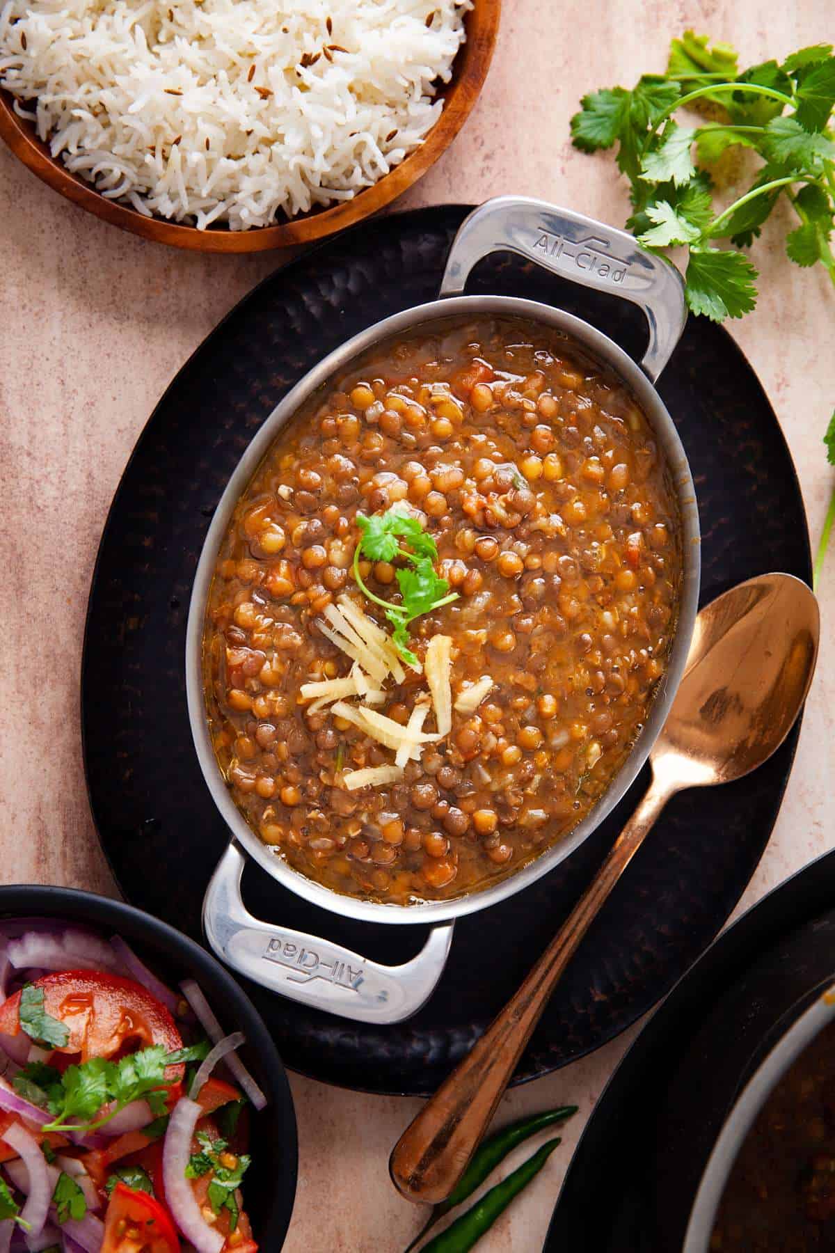 Whole Masoor Dal Served in an oval stainless steel dish and garnished with ginger juliennes and chopped cilantro.