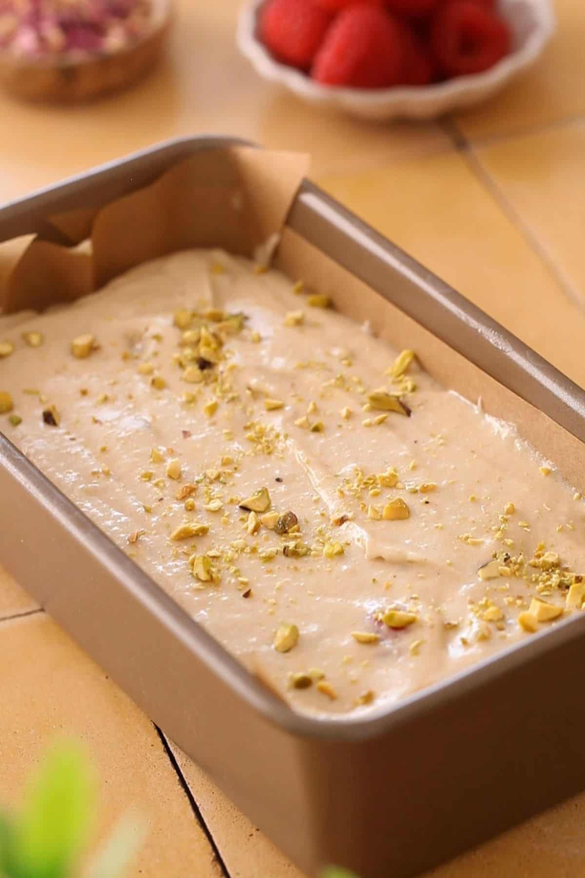 Rose water cake batter poured in loaf pan and sprinkled with pistachios.