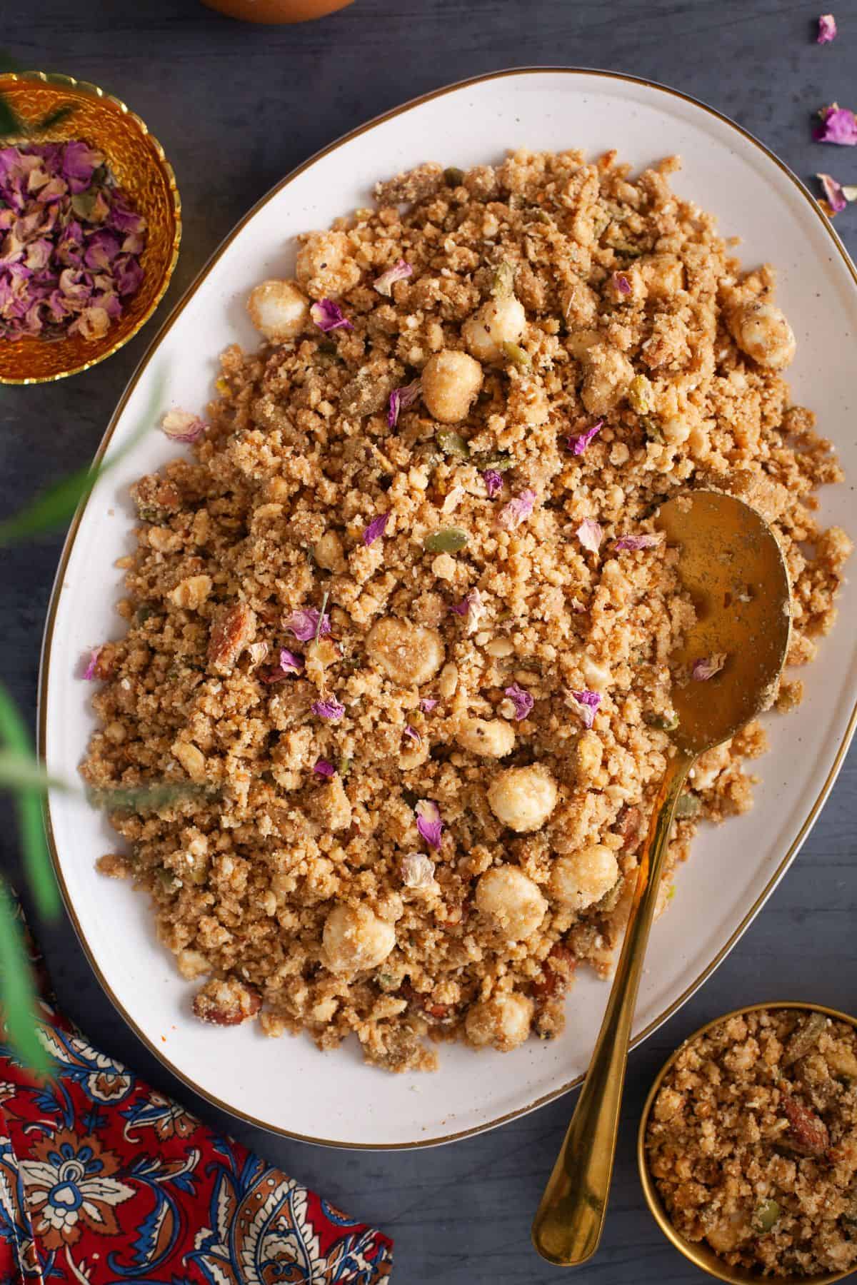 Sweet Panjiri served in a large white platter with a golden serving spoon.