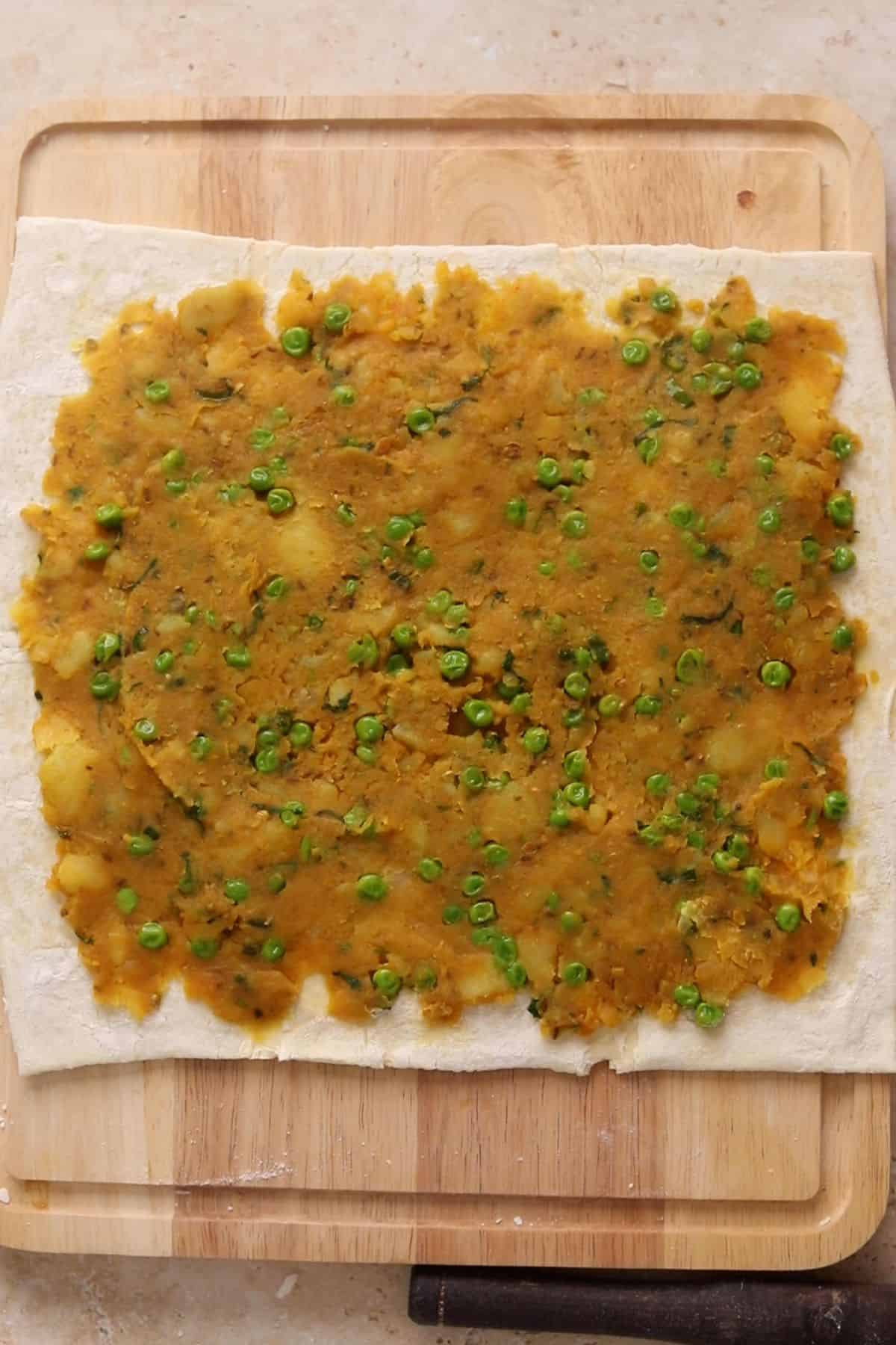Samosa filling is spread on a thawed puff pastry. 