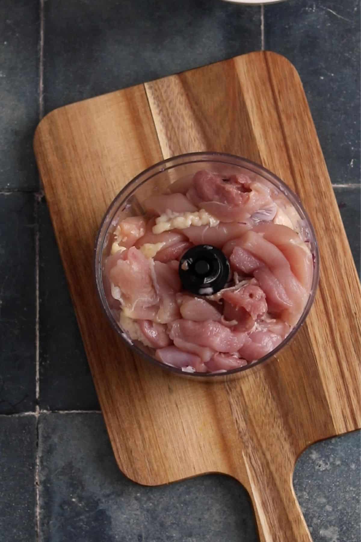 Roughly chopped chicken thighs in a chopper jar.
