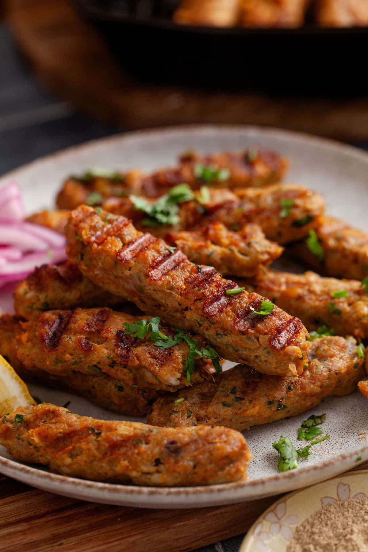 Side image of seekh kabab on a white stone plate.