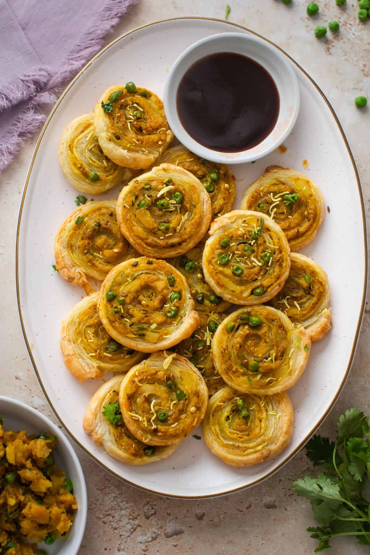 Potato & pea samosa pinwheels served with tamarind chutney on a cream plattter.