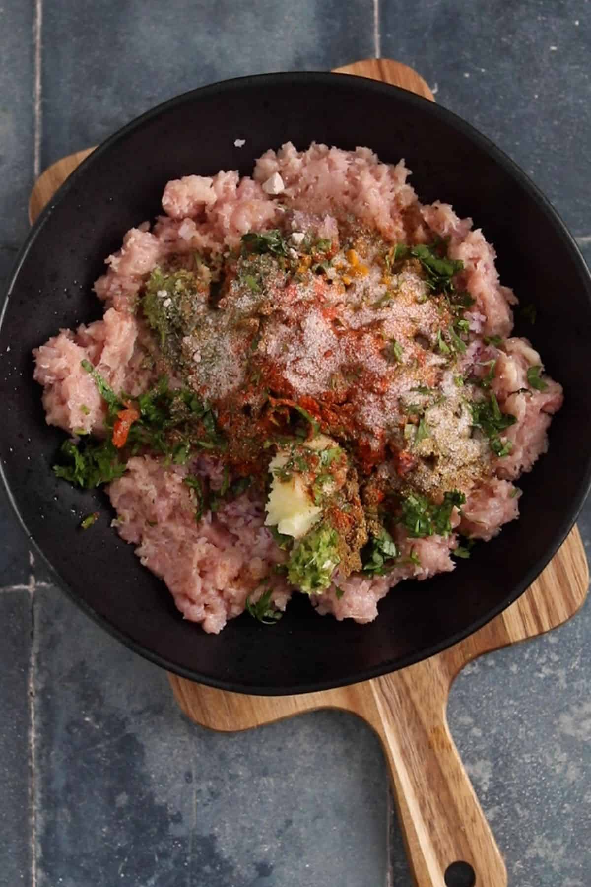 All the spices, aromatics, and herbs are added to minced chicken a alrge black bowl.