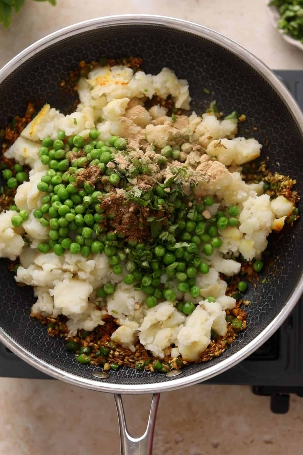Boiled potatoes, peas, cilantro and finsihsing spices are added to the skillet.