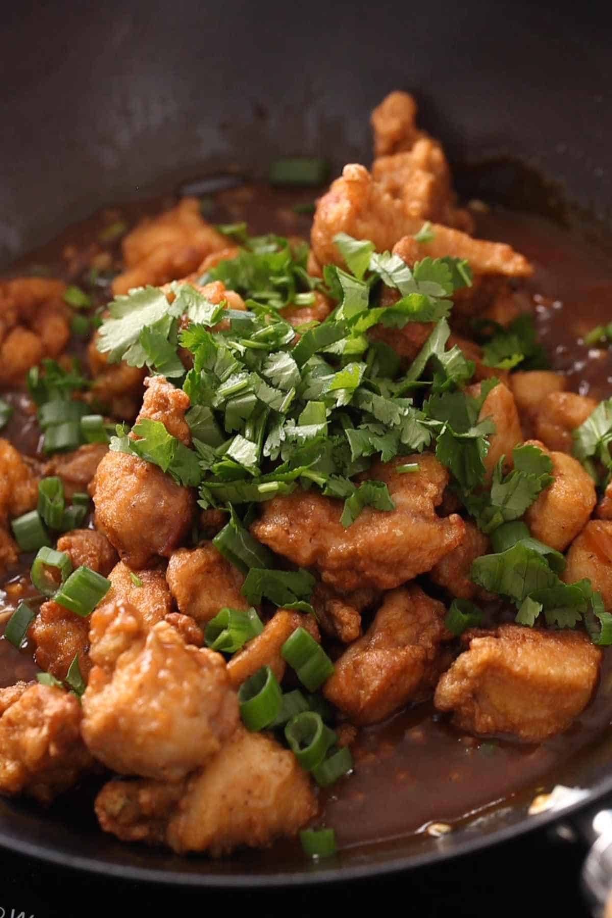 Adding crispy chicken, scallions and coriander to the manchurian sauce. 