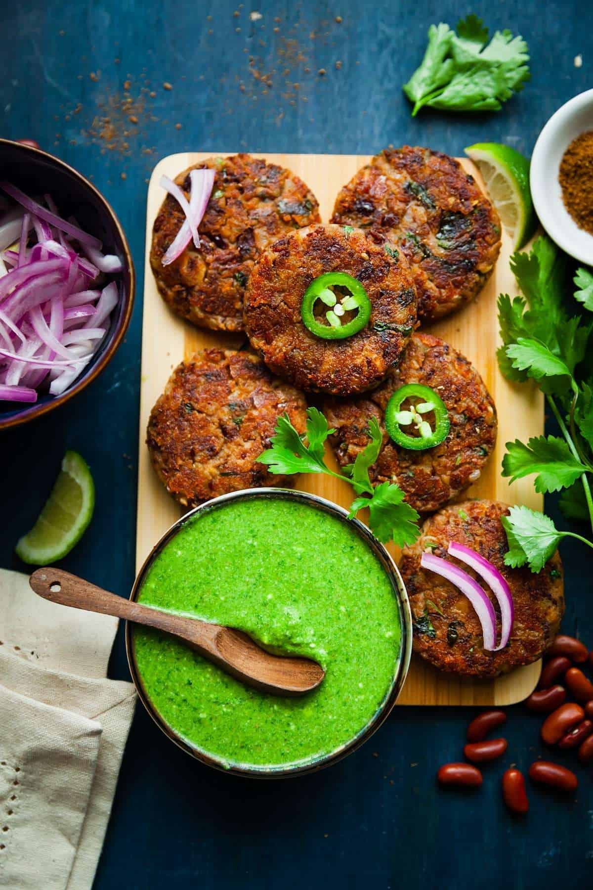 Vegan red kidney beans patties on a wooden board with green chutney and onions.