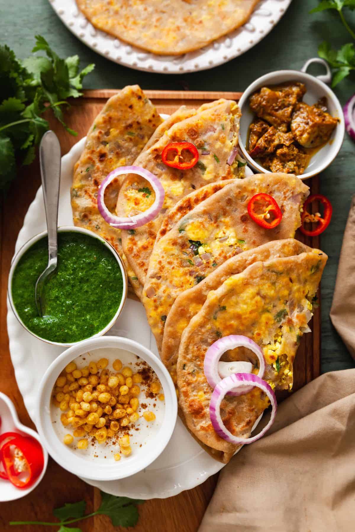 Stuffed paneer paratha on a white platter with pickles, yogurt and chutney. 
