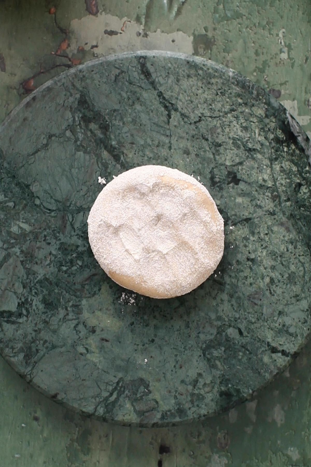 A dough ball is dusted with flour and placed on a granite rolling surface.