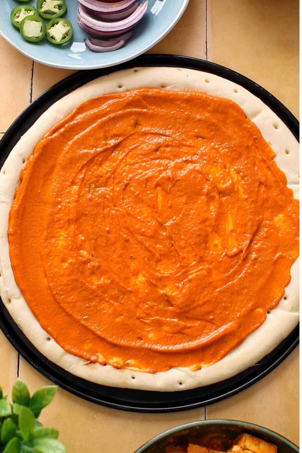 Makhani sauce is spread on pizza crust.