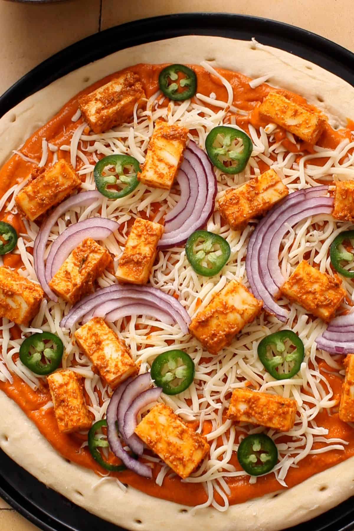 Paneer tikka, onuin and jalapenis are arranged on the pizza.