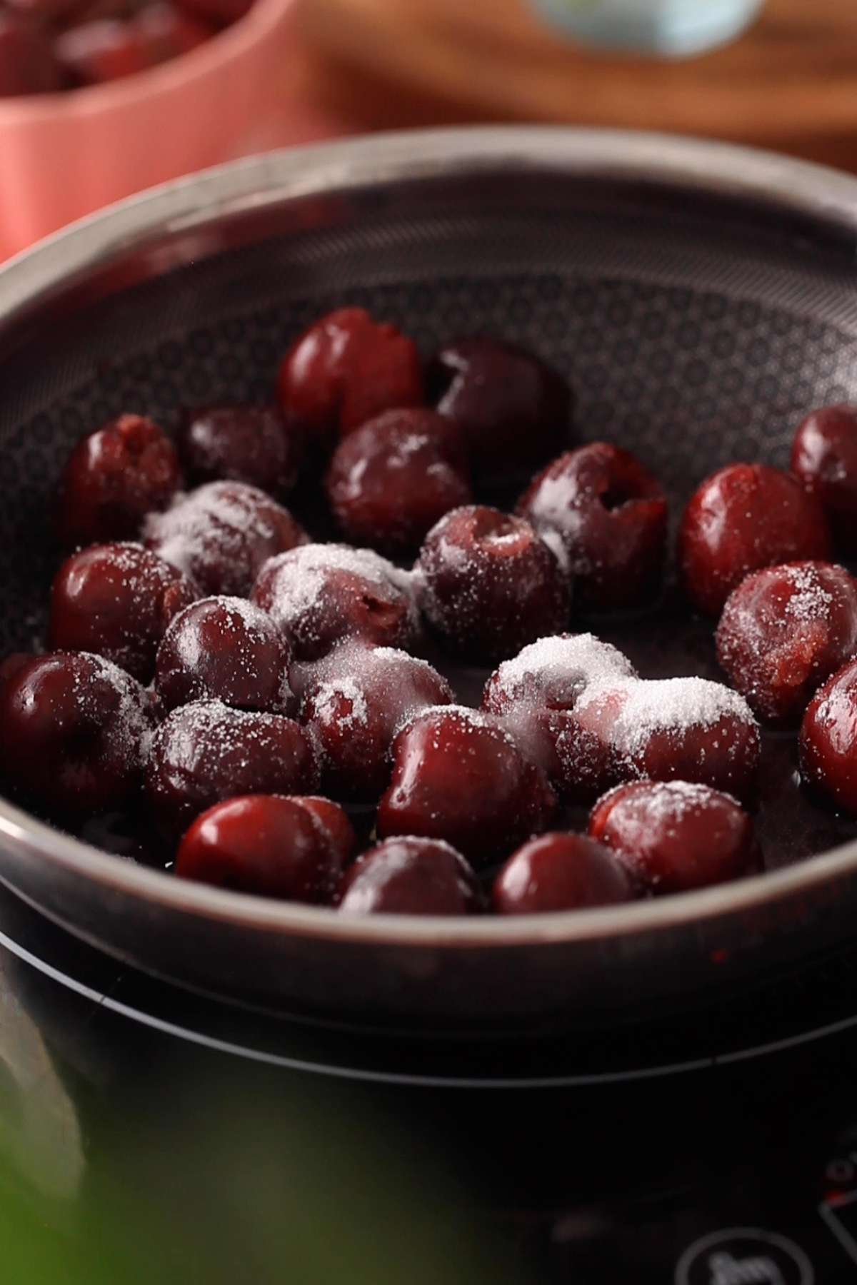 Fresh cherries, sugar and lemon in a black sauce pan.